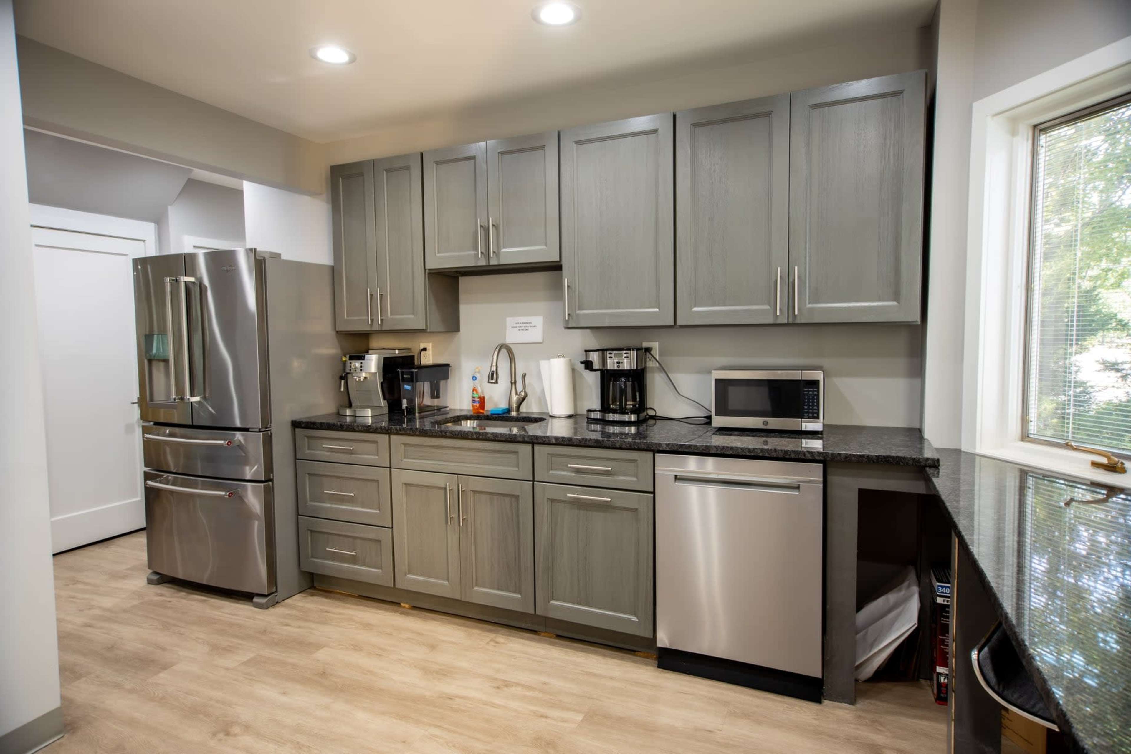A modern kitchen featuring gray cabinets, stainless steel appliances, and a dark granite countertop.