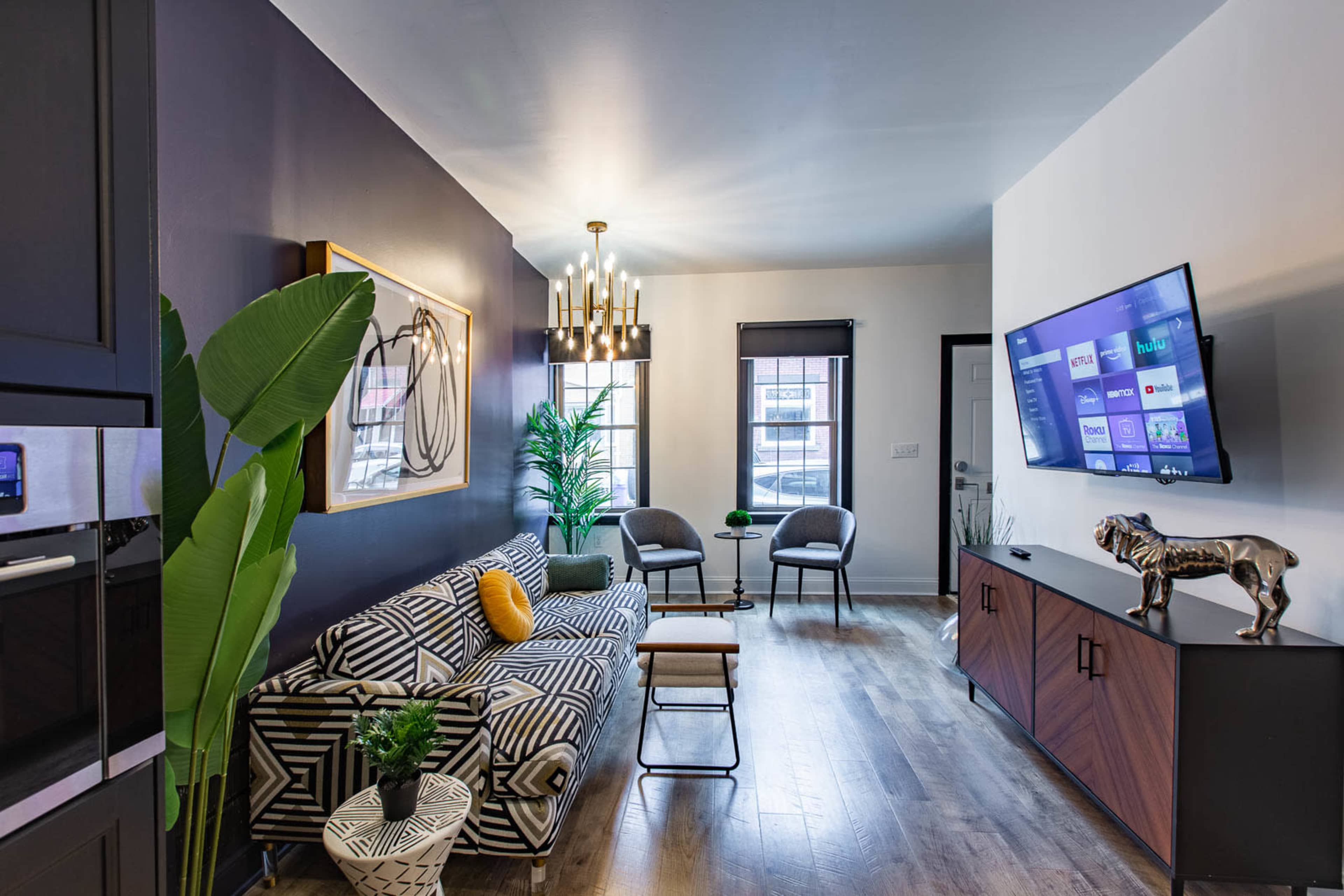 A modern living room with a striped sofa, a coffee table, a television mounted on a wall, and decorative plants.