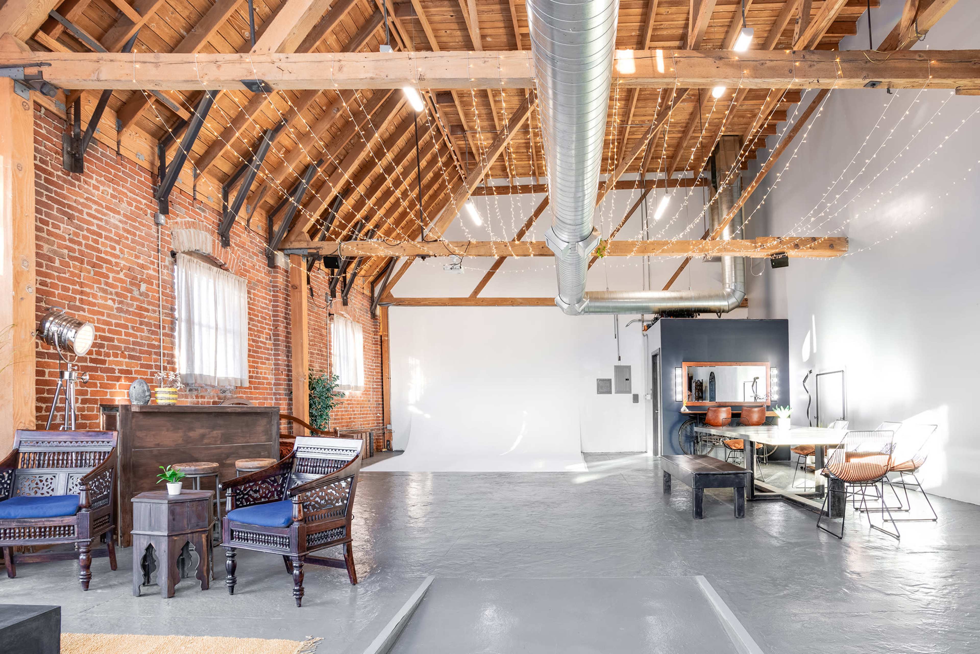 A spacious, industrial-style studio with a high wooden ceiling, exposed brick walls, and various seating and work areas.