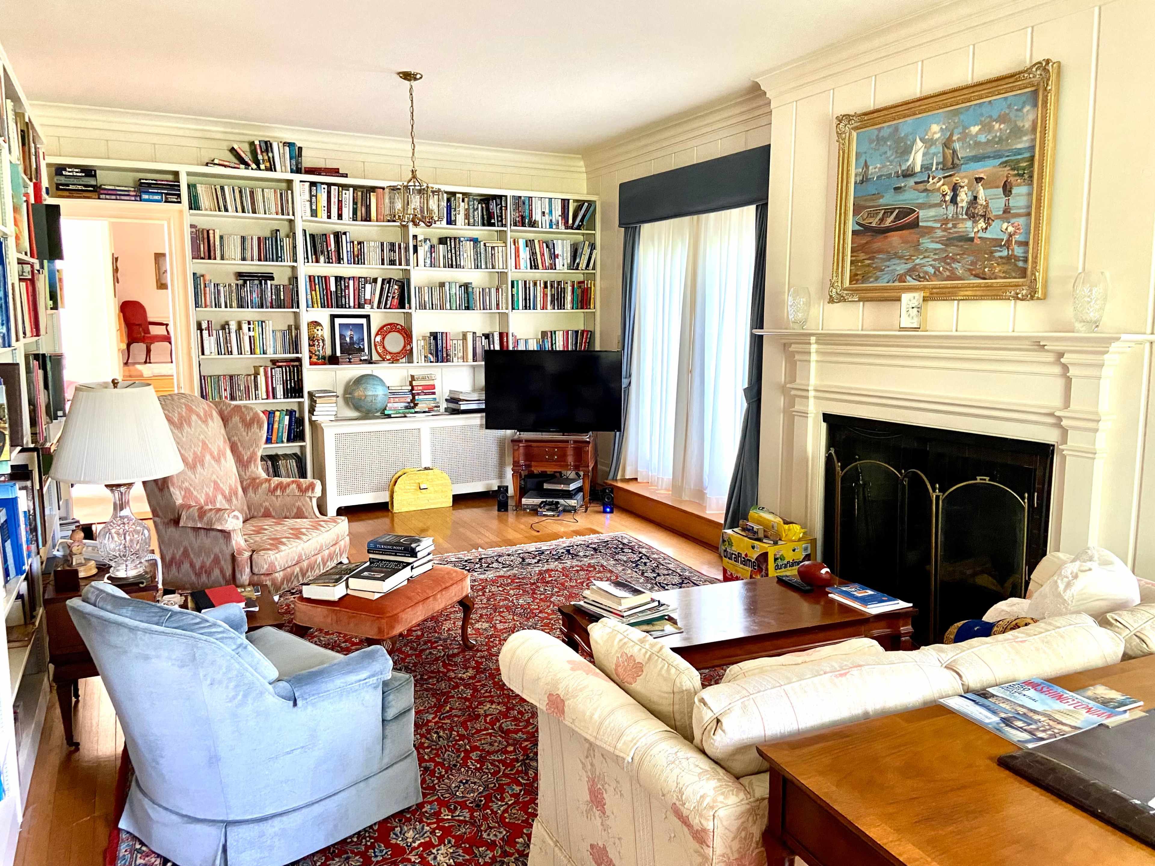 The living room features a large bookshelf filled with books, a fireplace, two sofas, a television, and various decorative items.