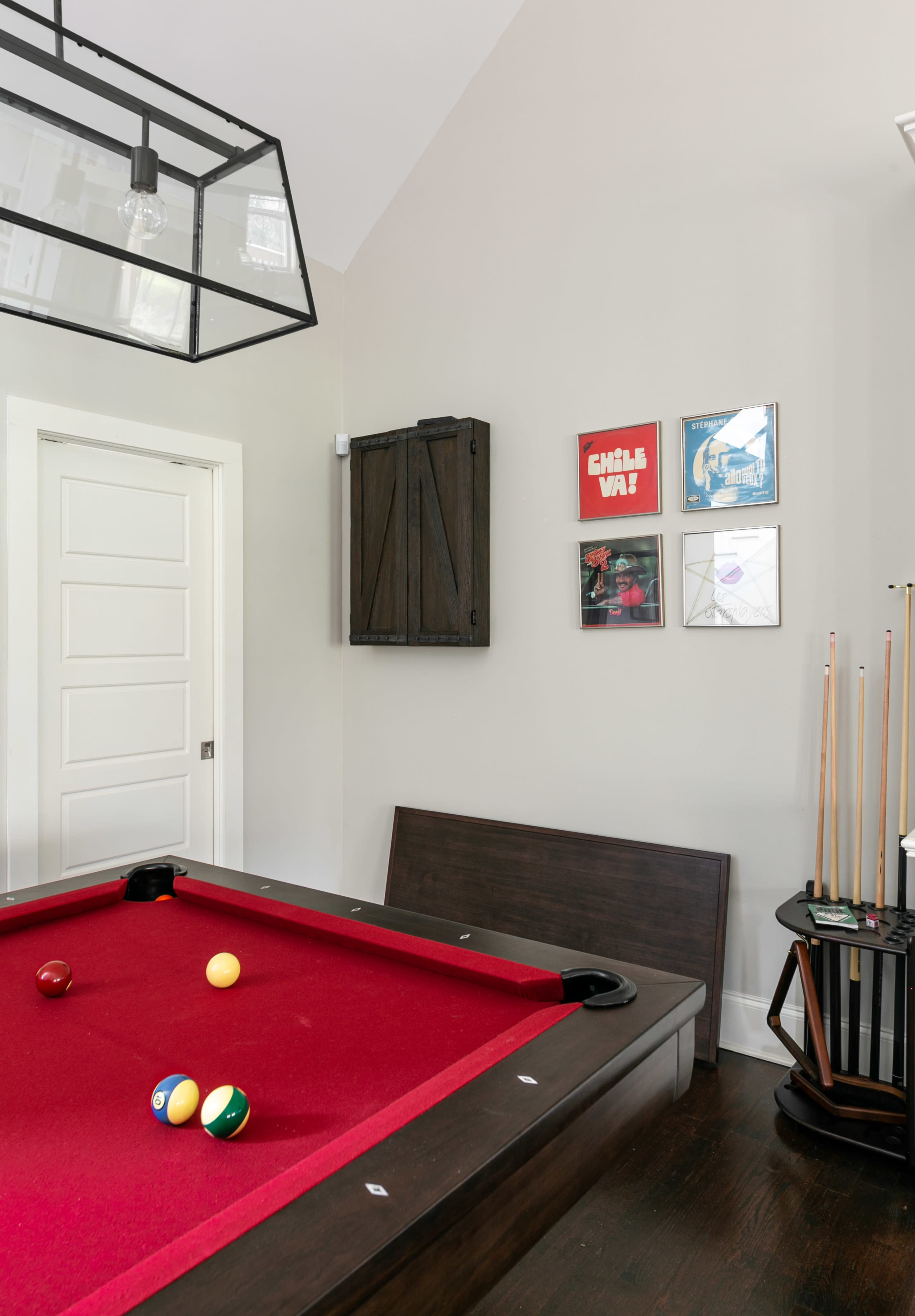 A room with a red pool table, a door, and framed artwork on the wall.