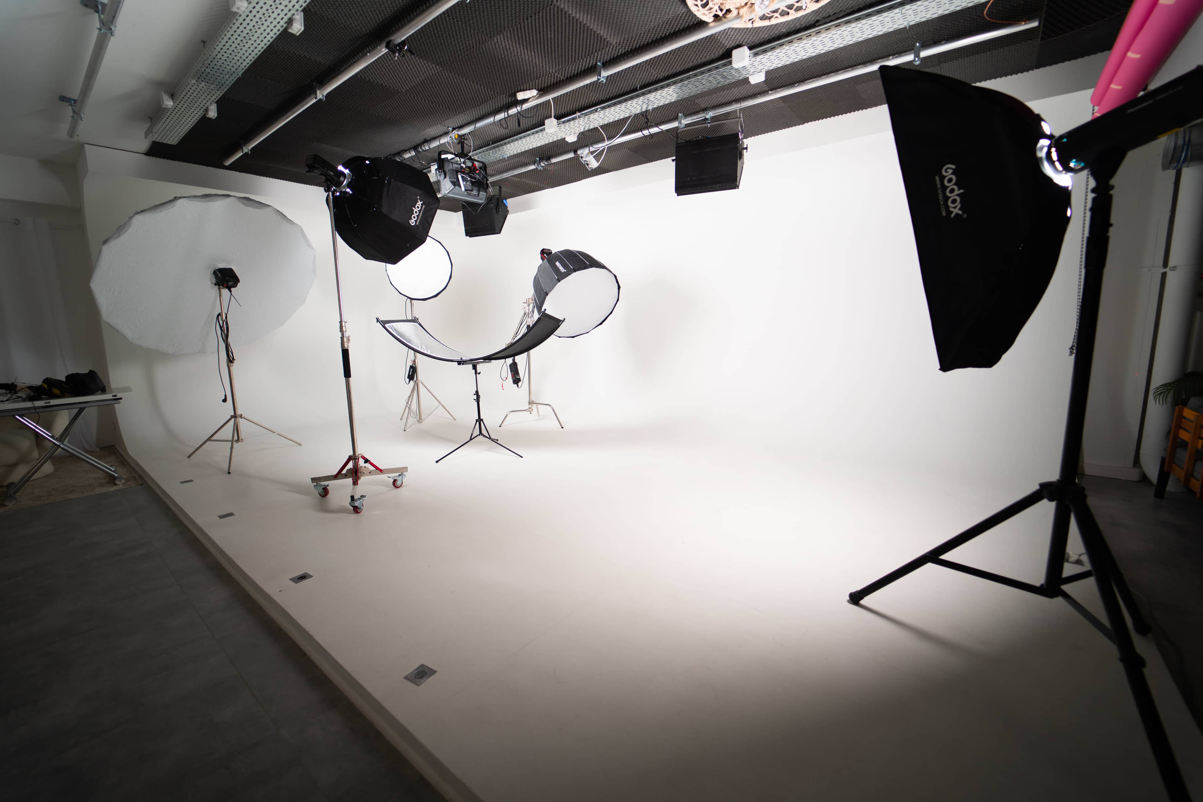 A photography studio with a plain white backdrop, lighting equipment, and a curved chair set up in the center.