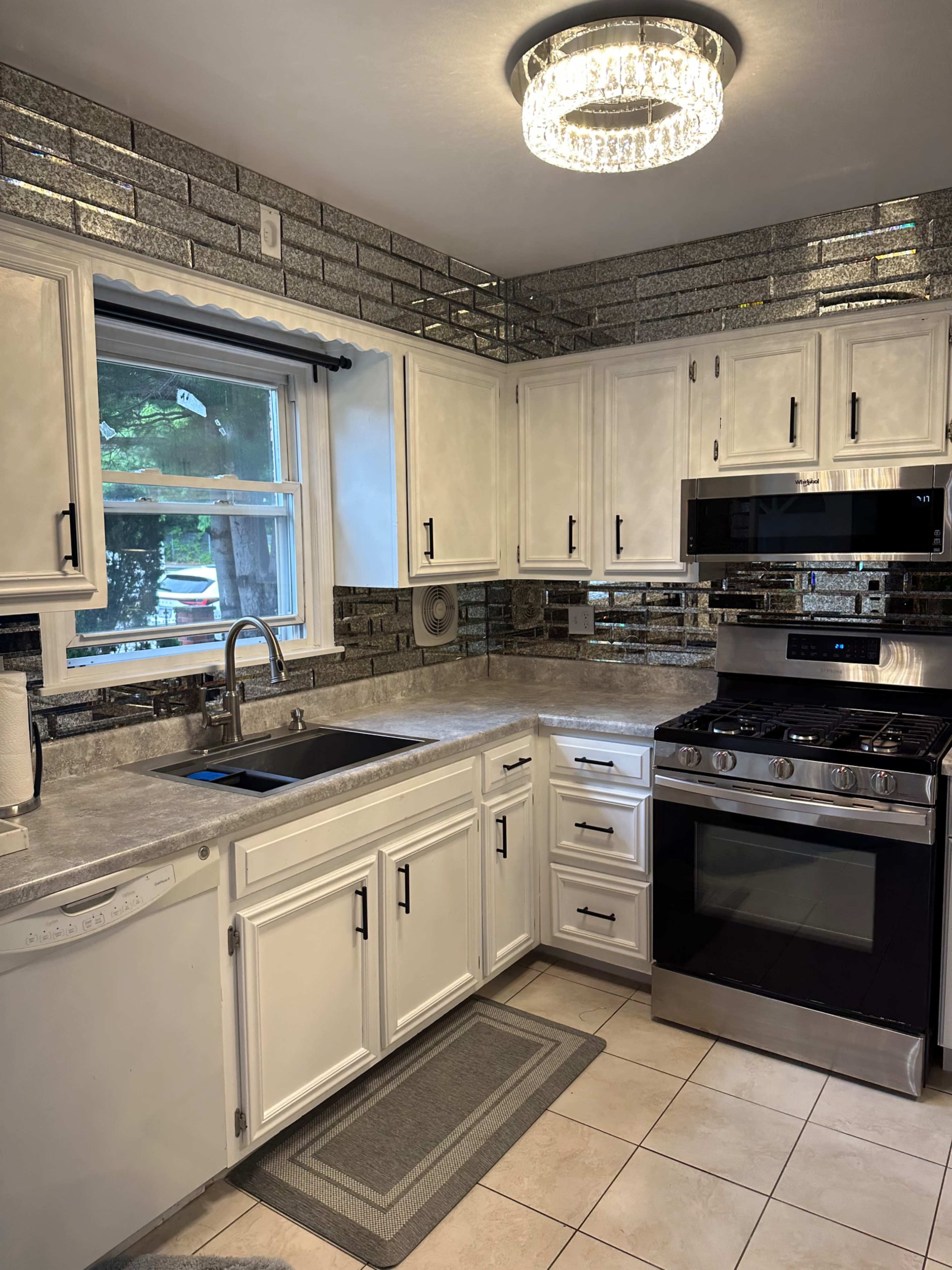 A modern kitchen with white cabinets, a stainless steel stove, and a mirrored backsplash.