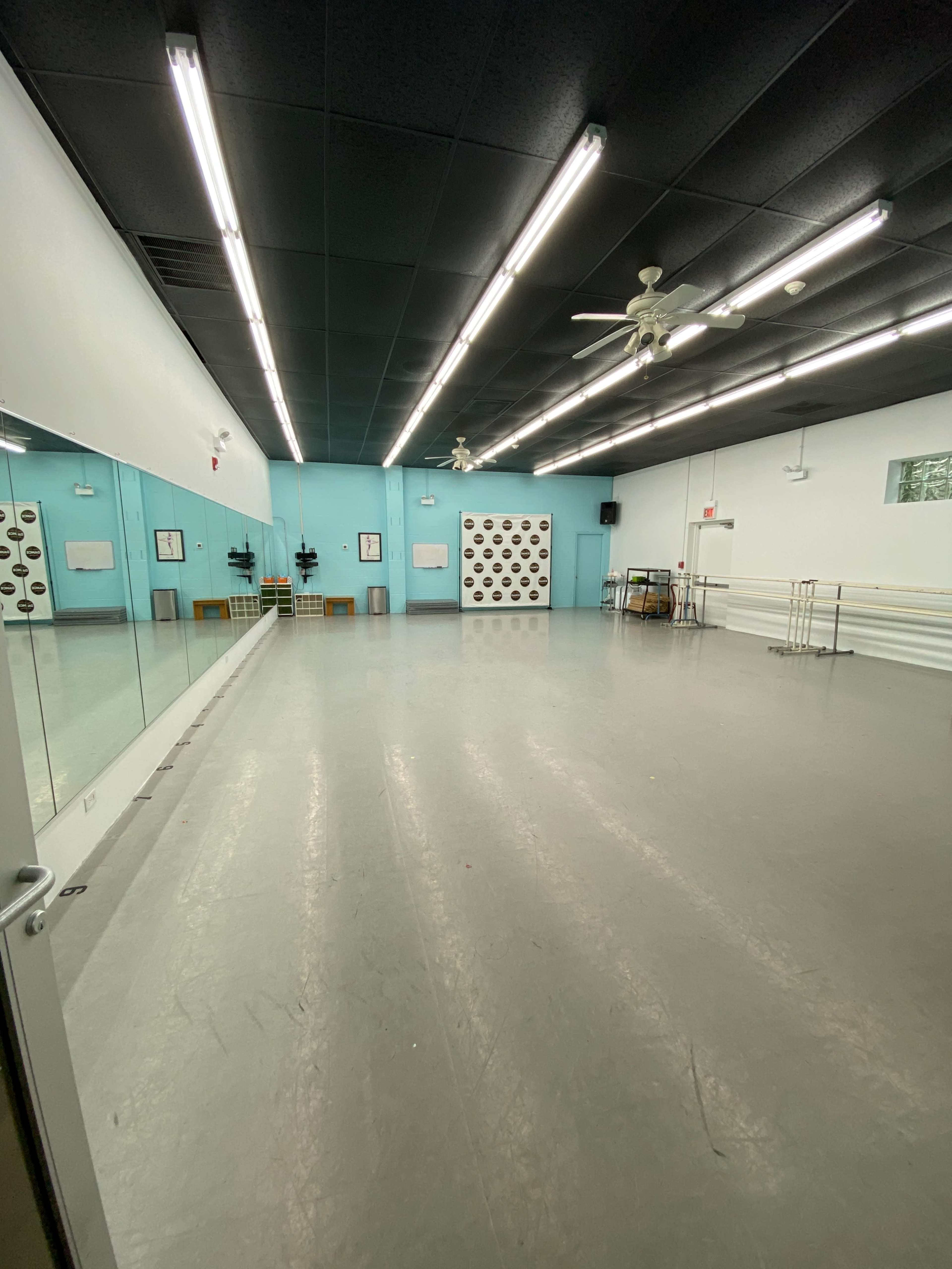 A spacious dance studio with a mirrored wall, gray flooring, and a light blue accent wall adorned with black polka dots.