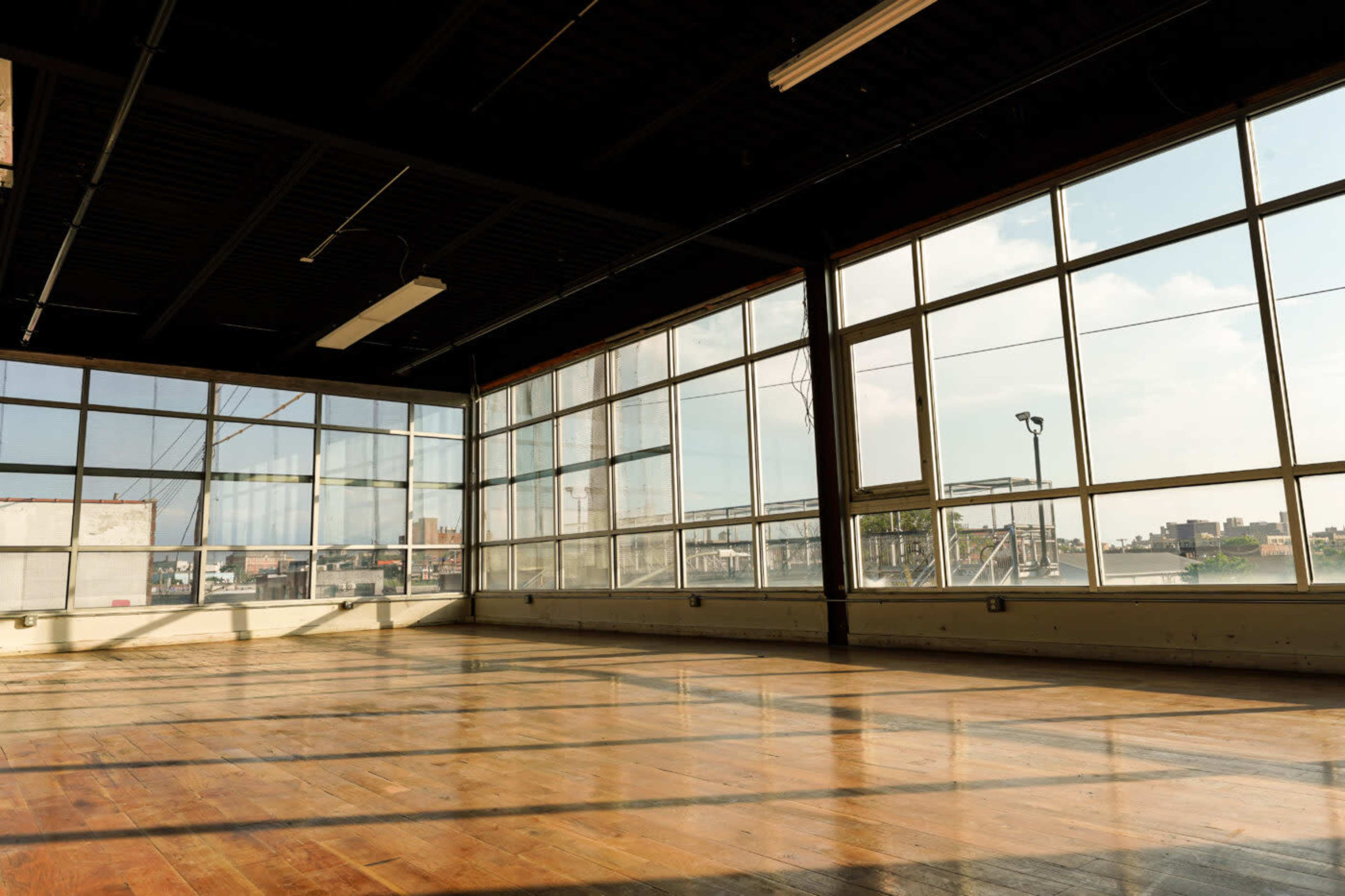An empty room with large windows allowing natural light to illuminate the polished wooden floor.
