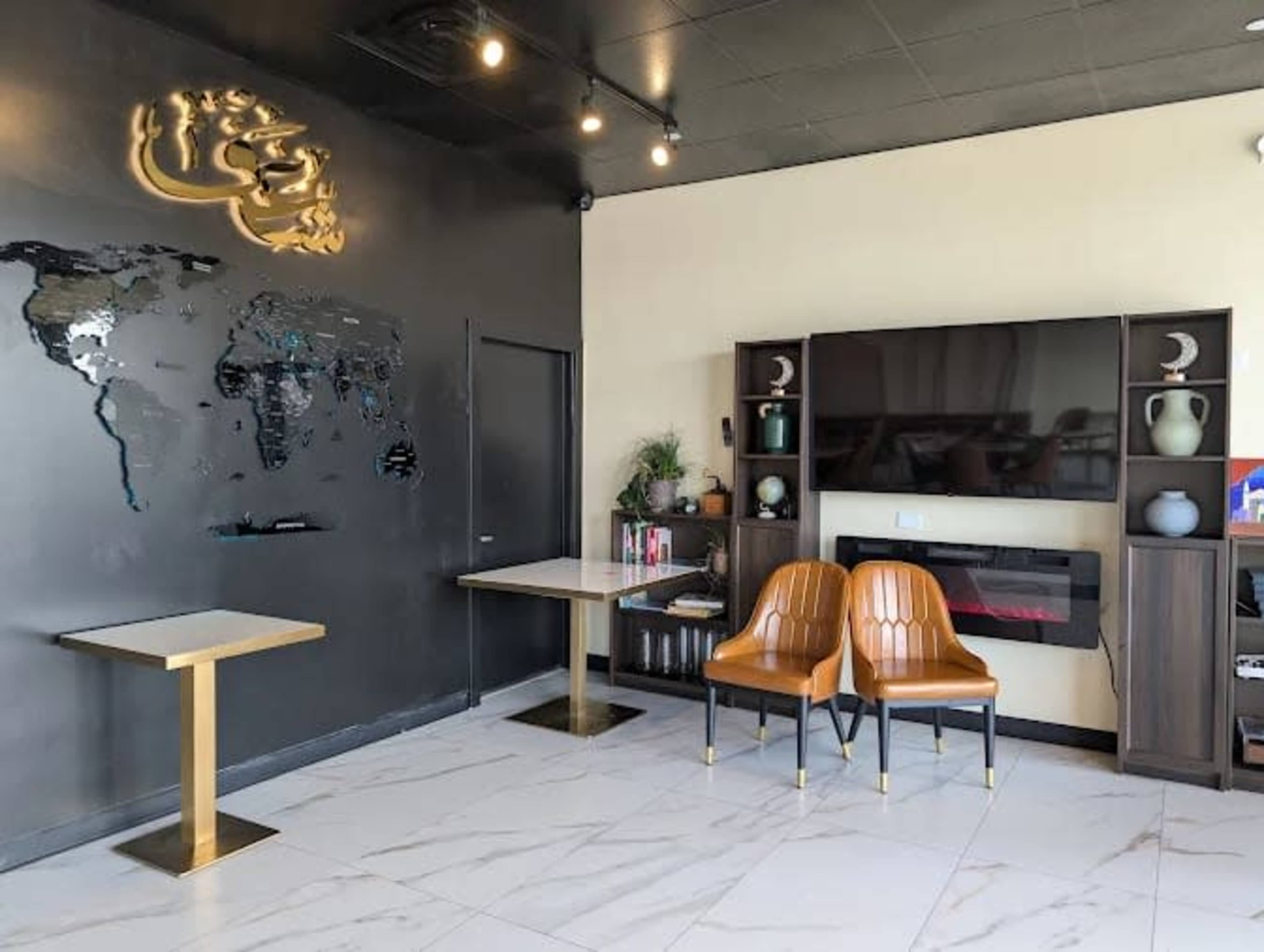 The image shows a modern waiting area featuring two brown chairs, a wall with a world map design, and a sleek table next to a wall-mounted television.