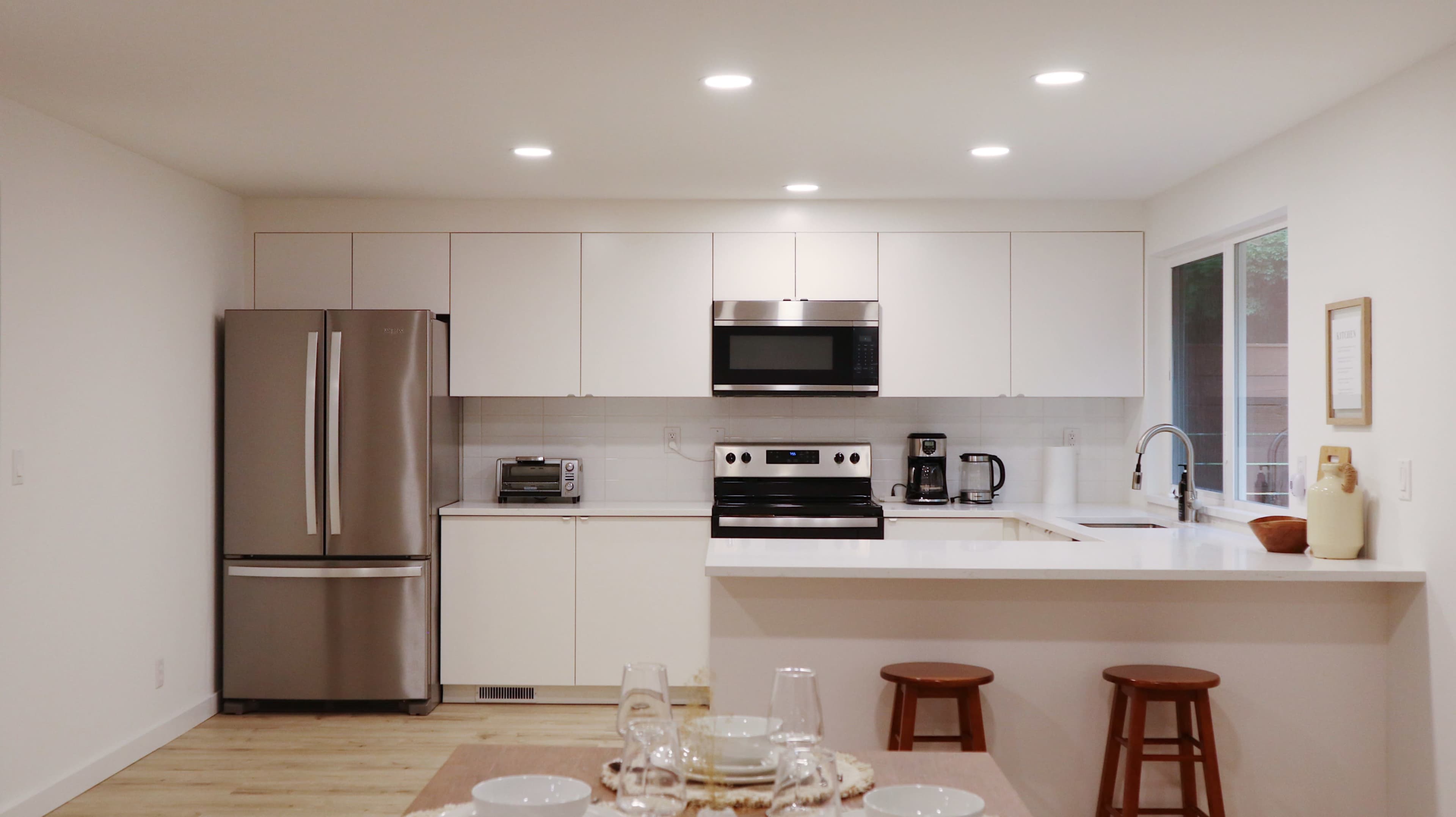 A modern kitchen with stainless steel appliances, white cabinetry, and a countertop with two wooden stools.