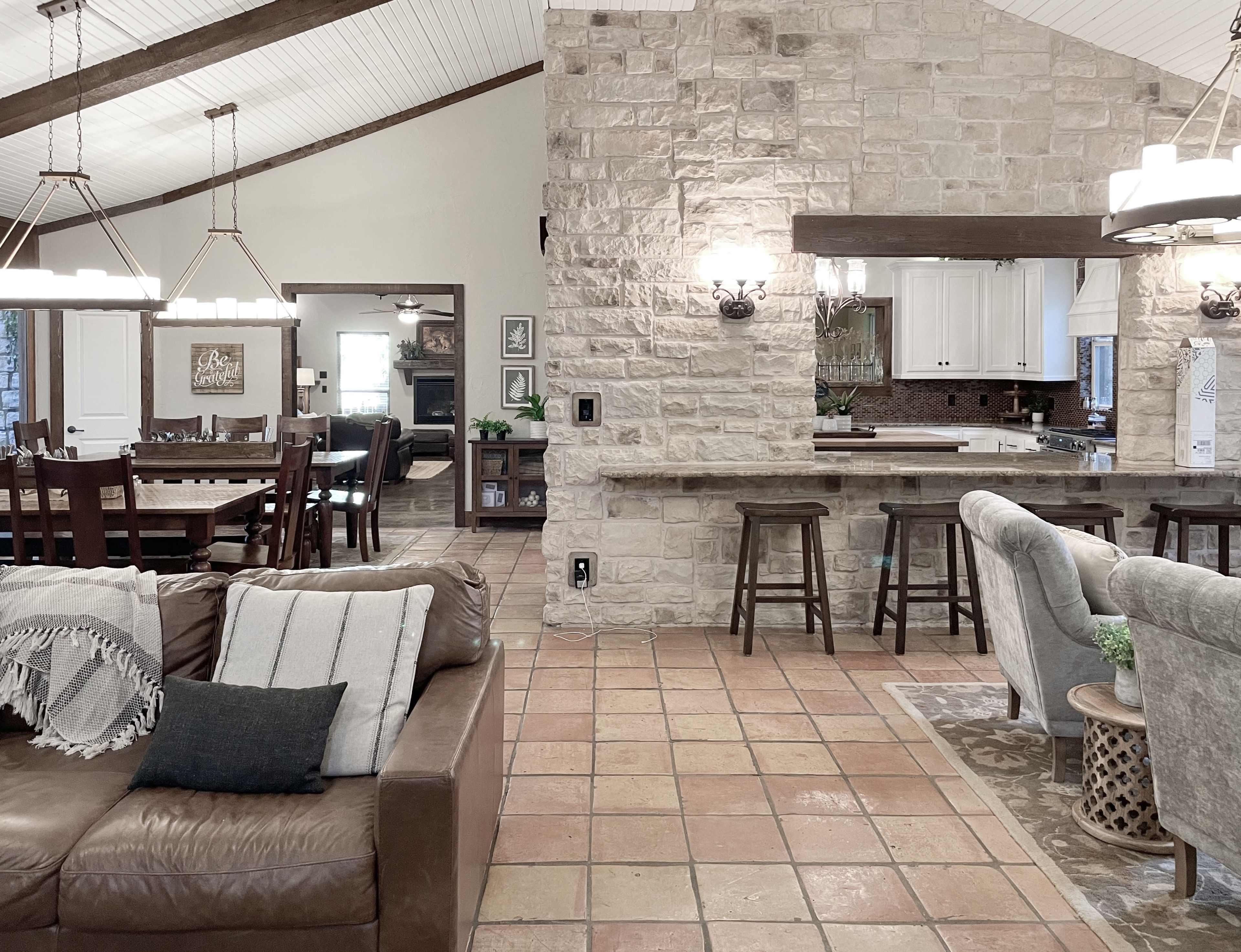An open-concept living area with a stone wall, a kitchen bar with stools, and a dining area featuring wooden tables and chairs.