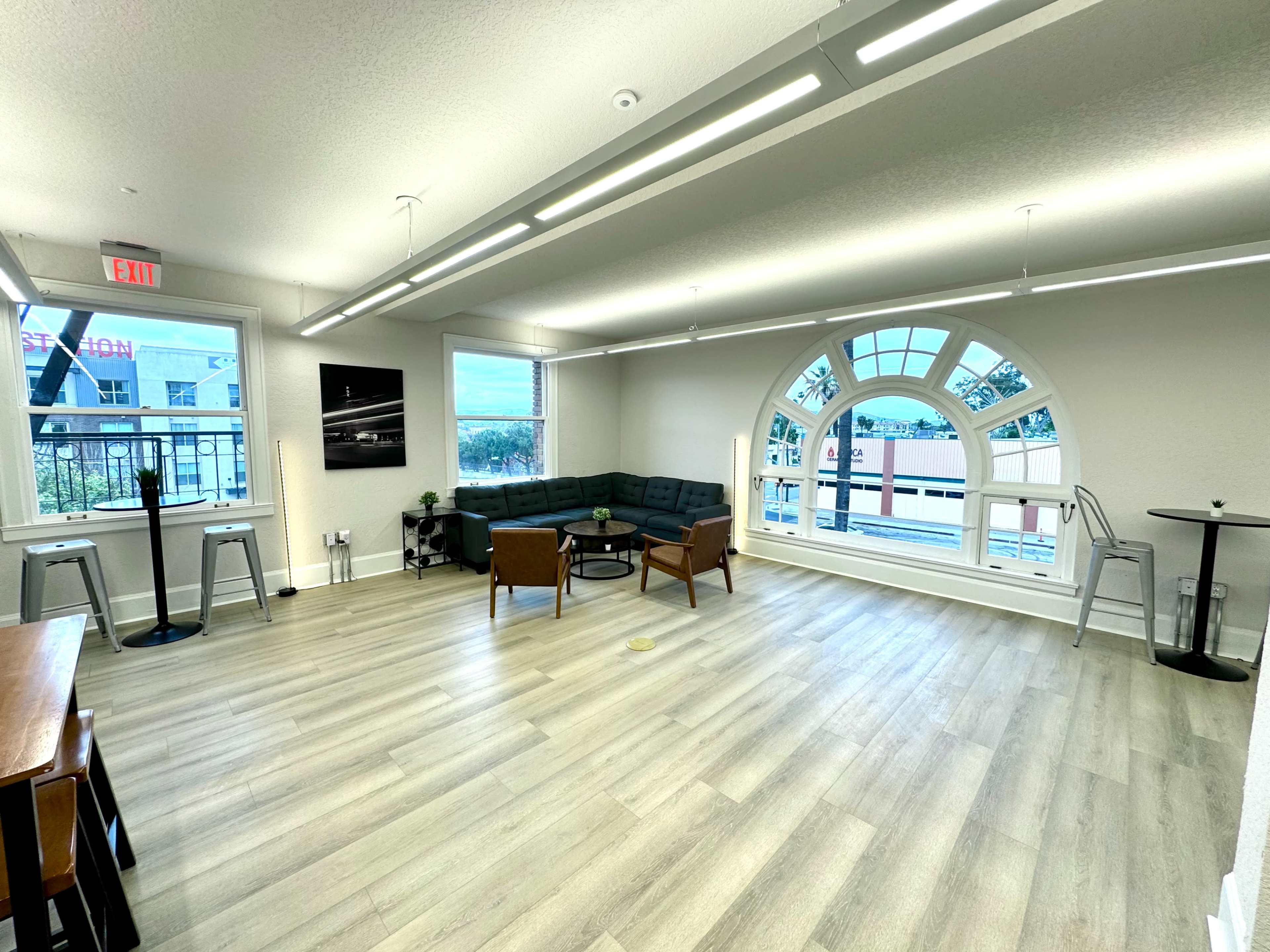 A modern, bright office space with large windows, a sectional couch, and several small tables.