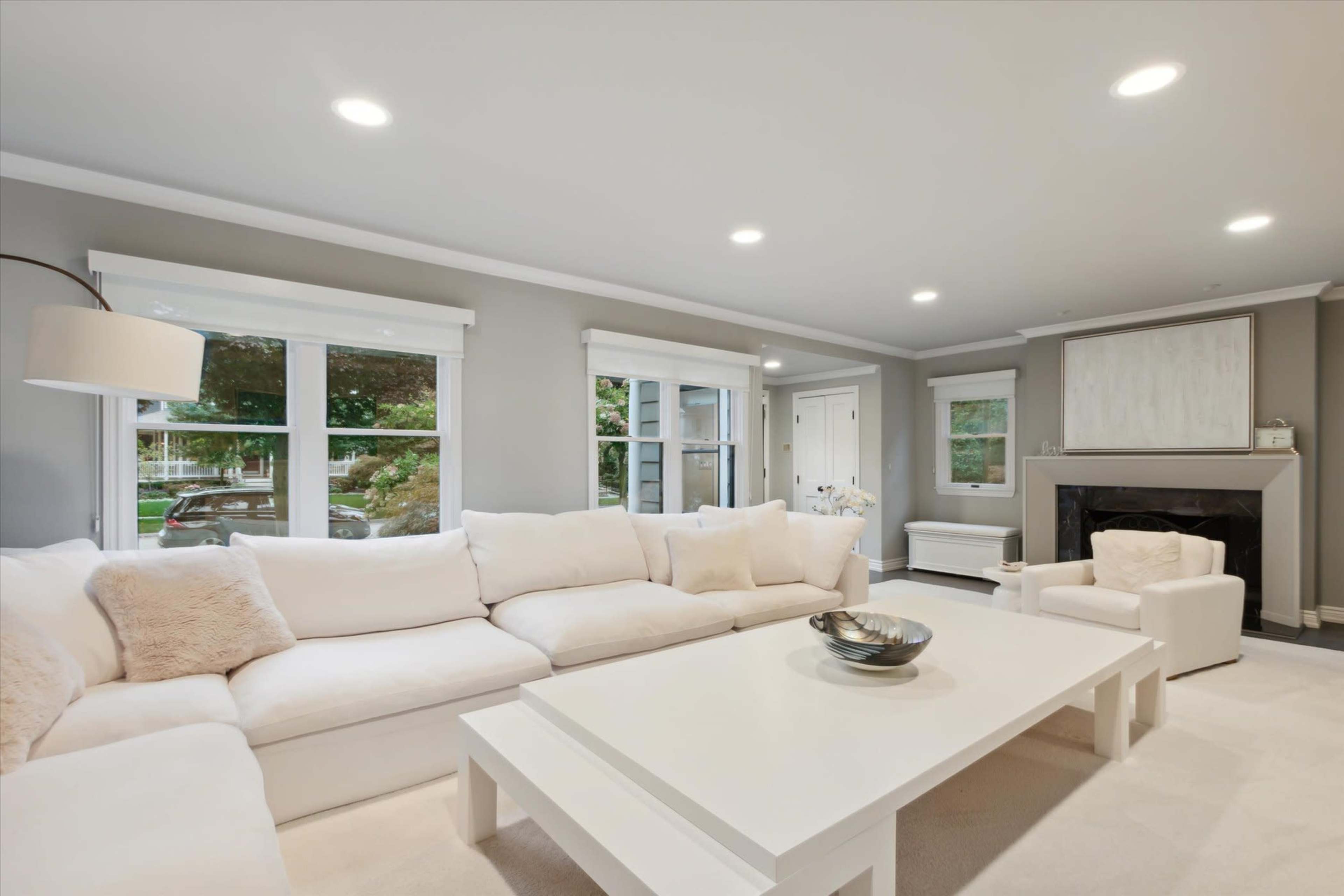A modern living room featuring a large white sectional sofa, a coffee table, and a fireplace, with natural light coming through the windows.