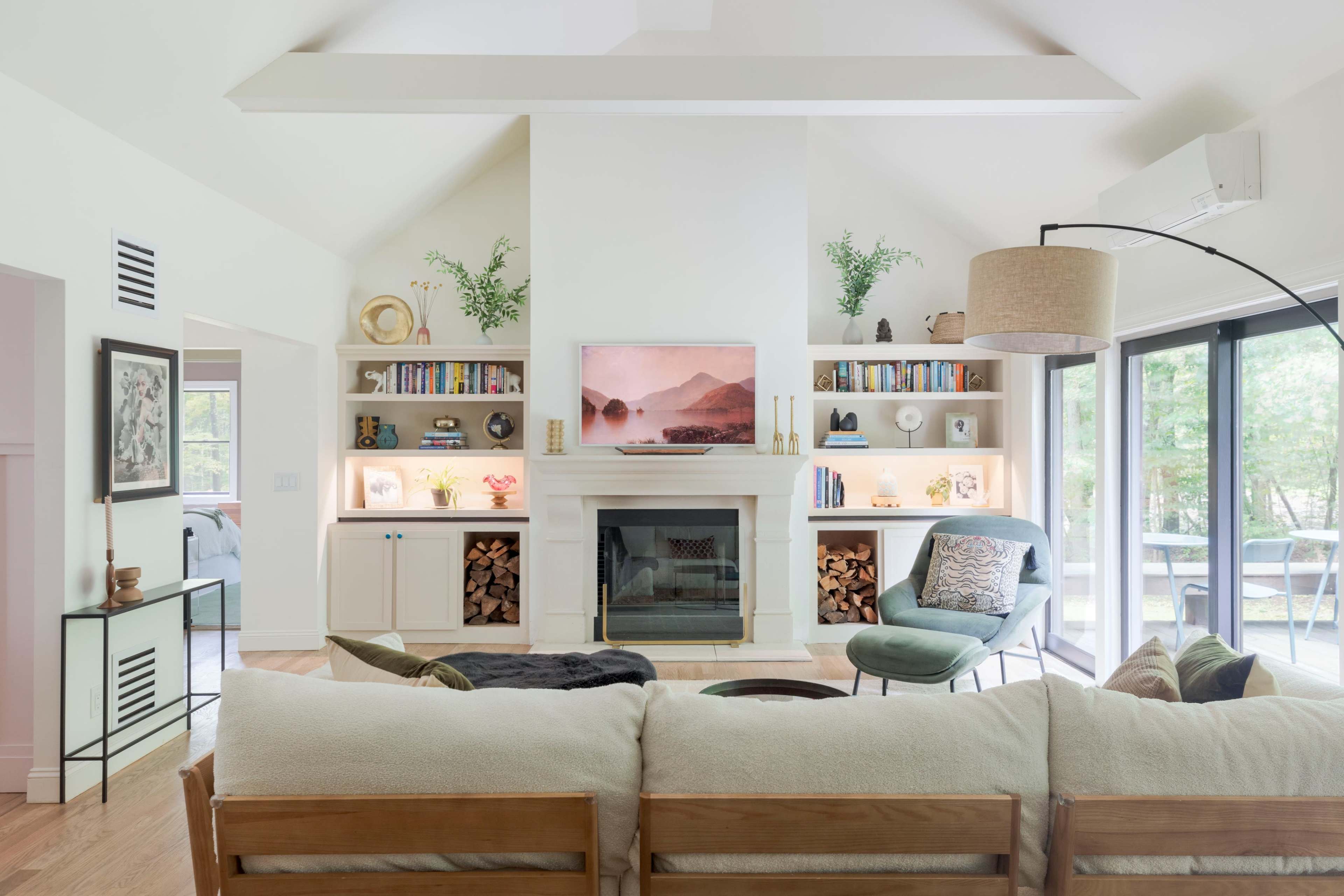 A bright, modern living room features a central fireplace with built-in shelves on either side, a comfortable couch, and large windows offering a view of the outdoor space.