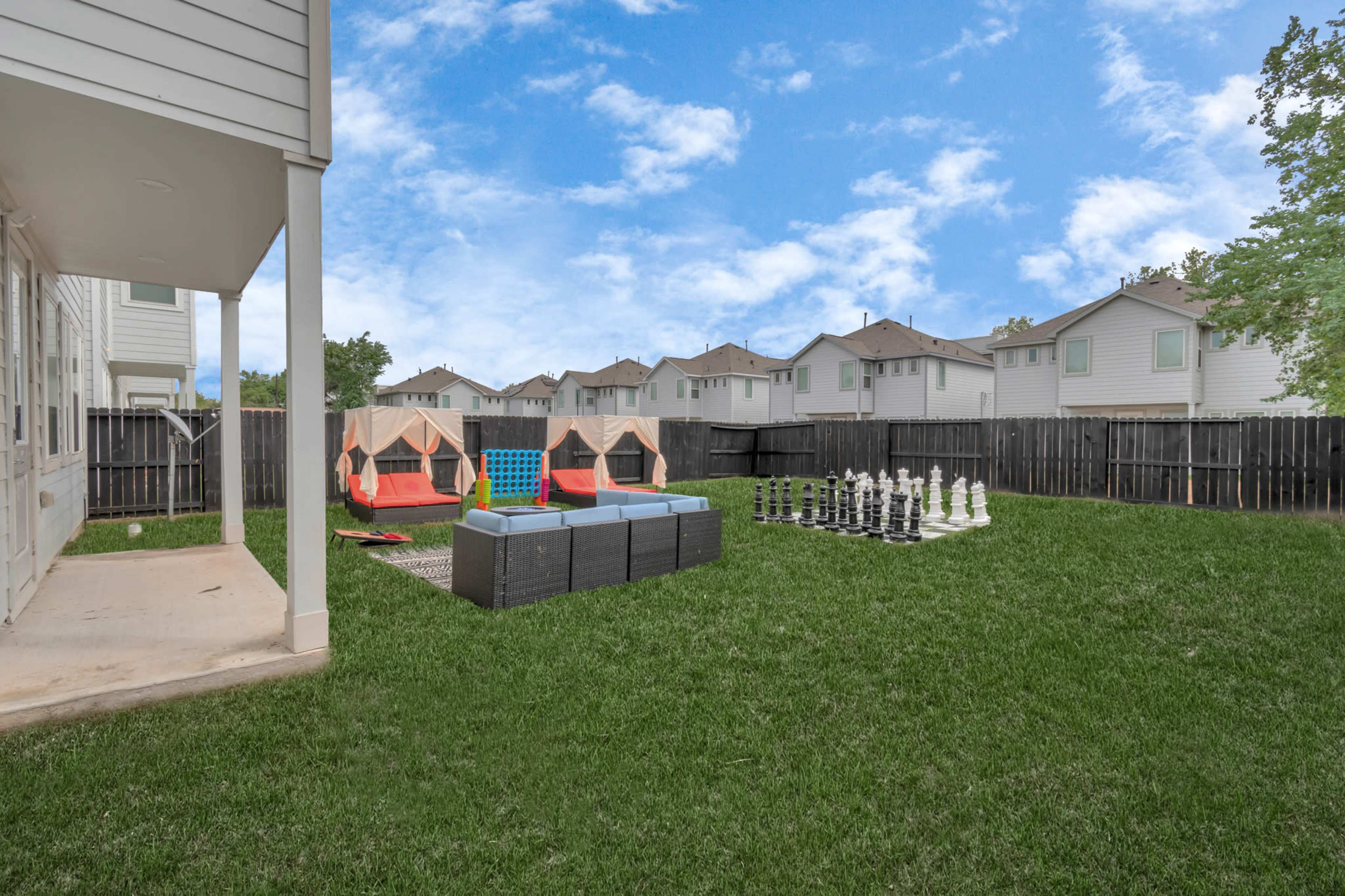 A backyard with two red and blue lounge chairs, a large chess set, and several tents, surrounded by a green lawn and lined by wooden fences.