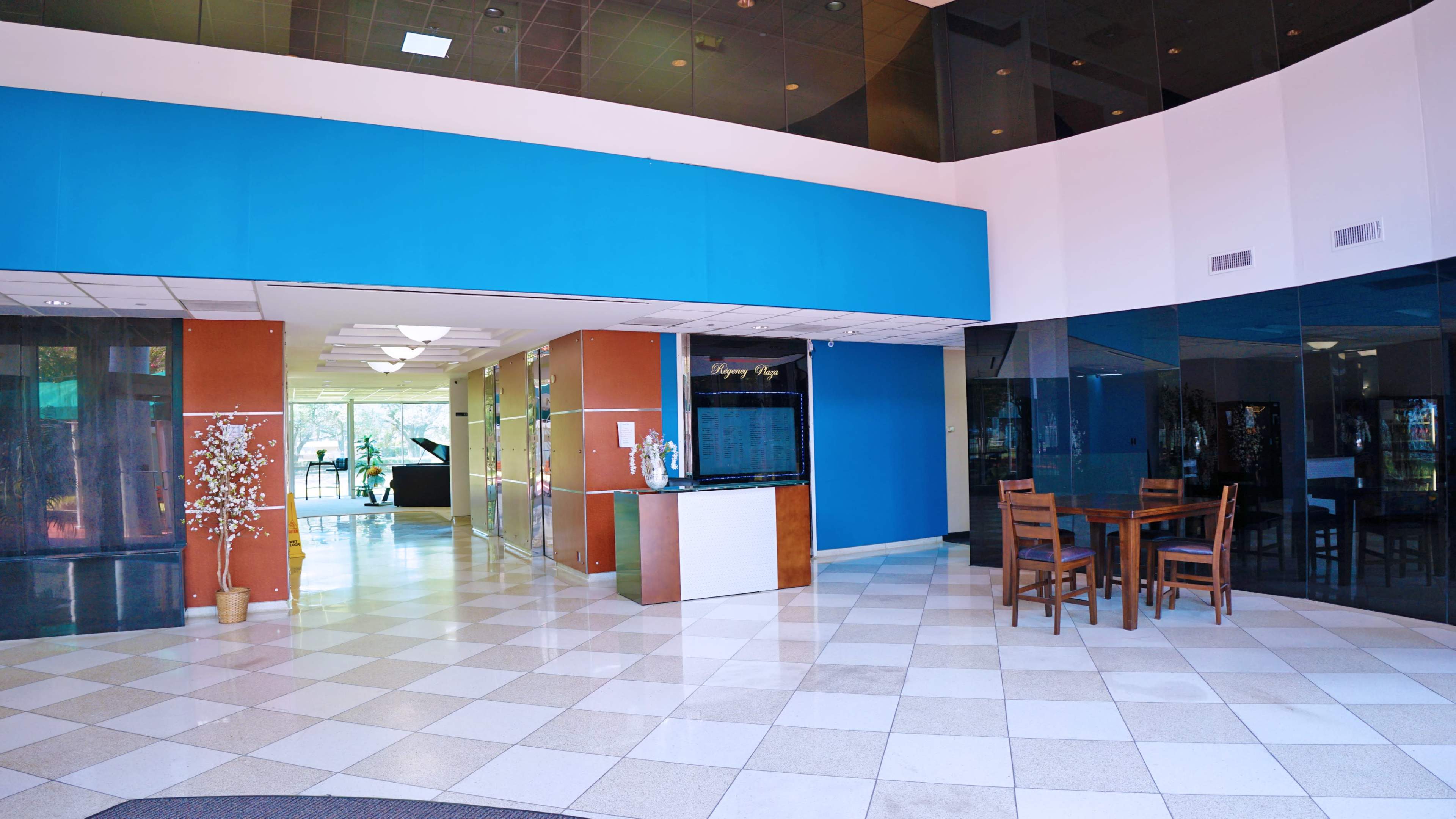 A spacious lobby area featuring a reception desk, seating area with chairs, and large glass windows.