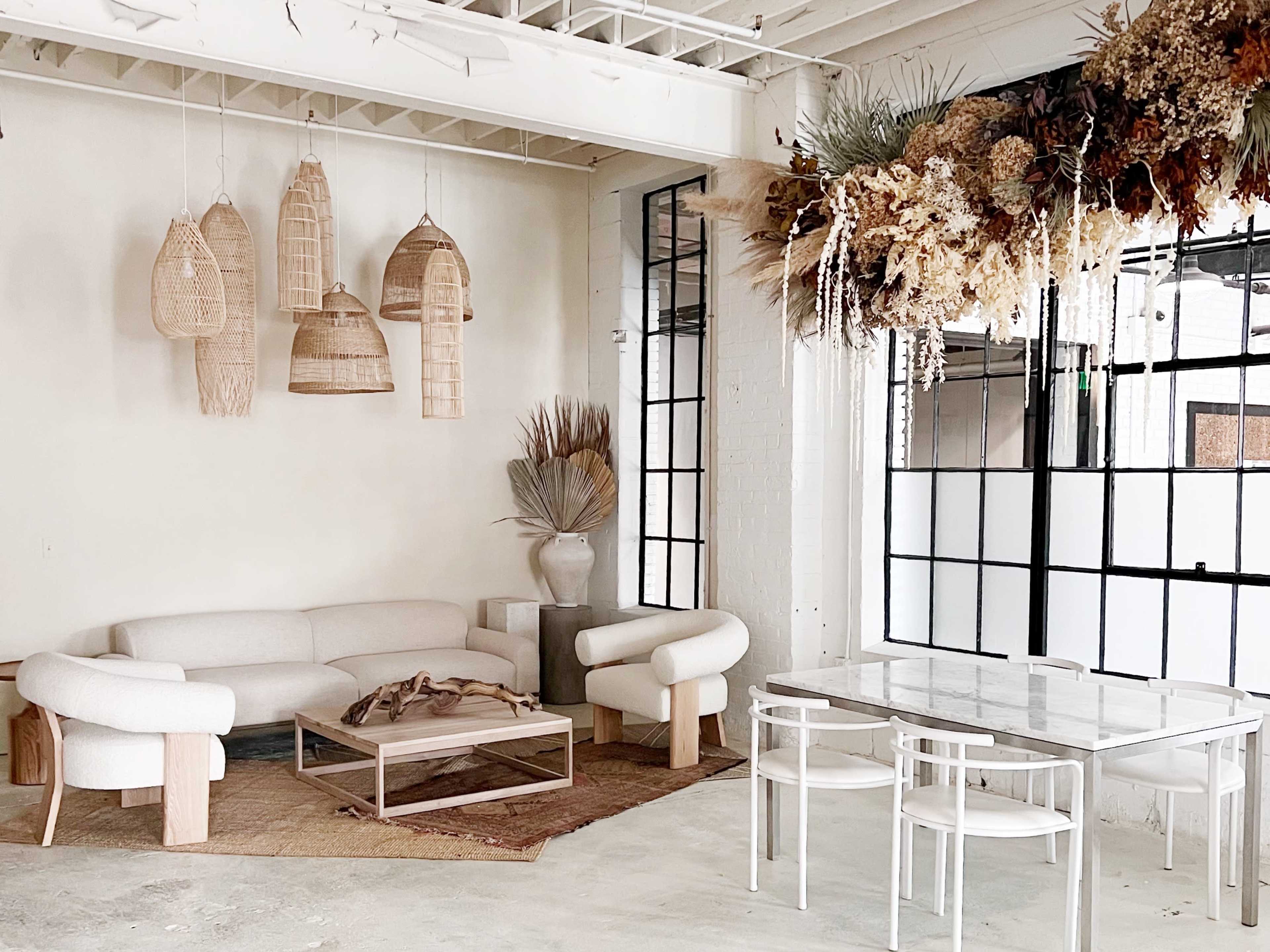 The image shows a modern, minimalist interior featuring a light-colored lounge area with a sofa and unique hanging decor, alongside a dining table with clear chairs.