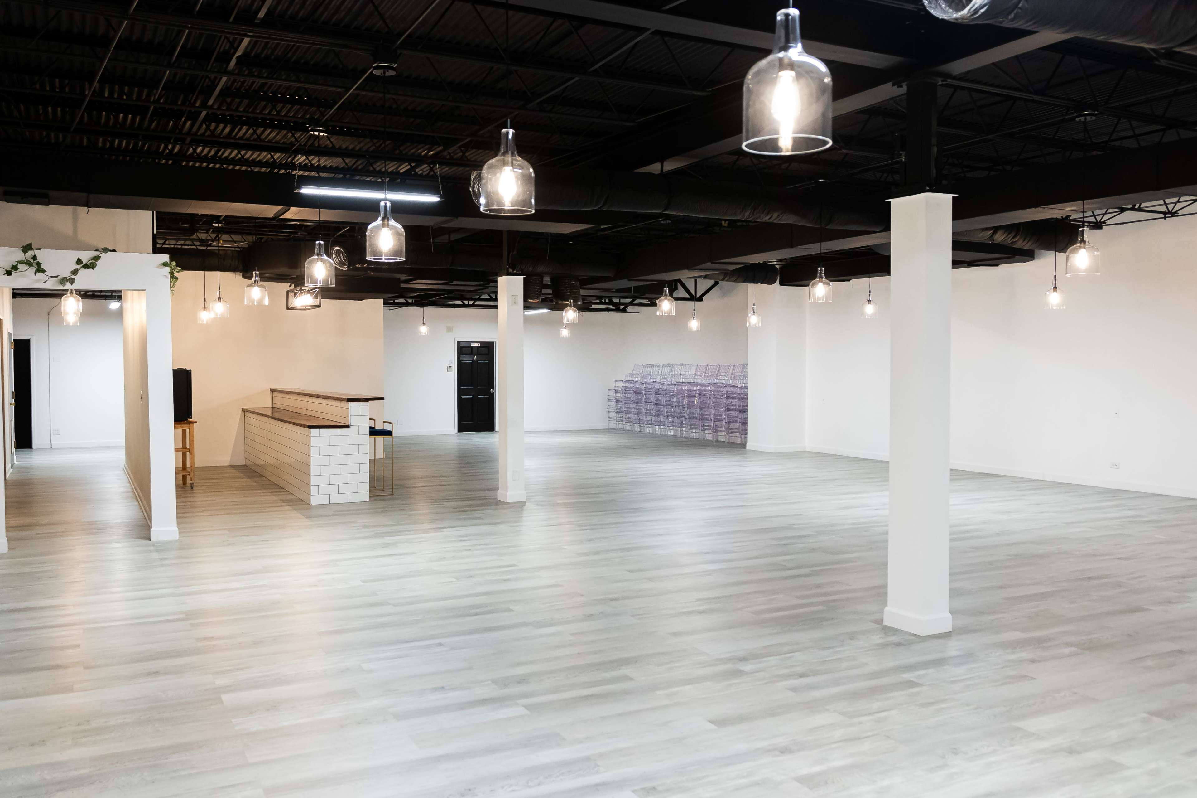 The image shows a spacious, empty commercial interior with light-colored flooring, white walls, and hanging pendant lights.