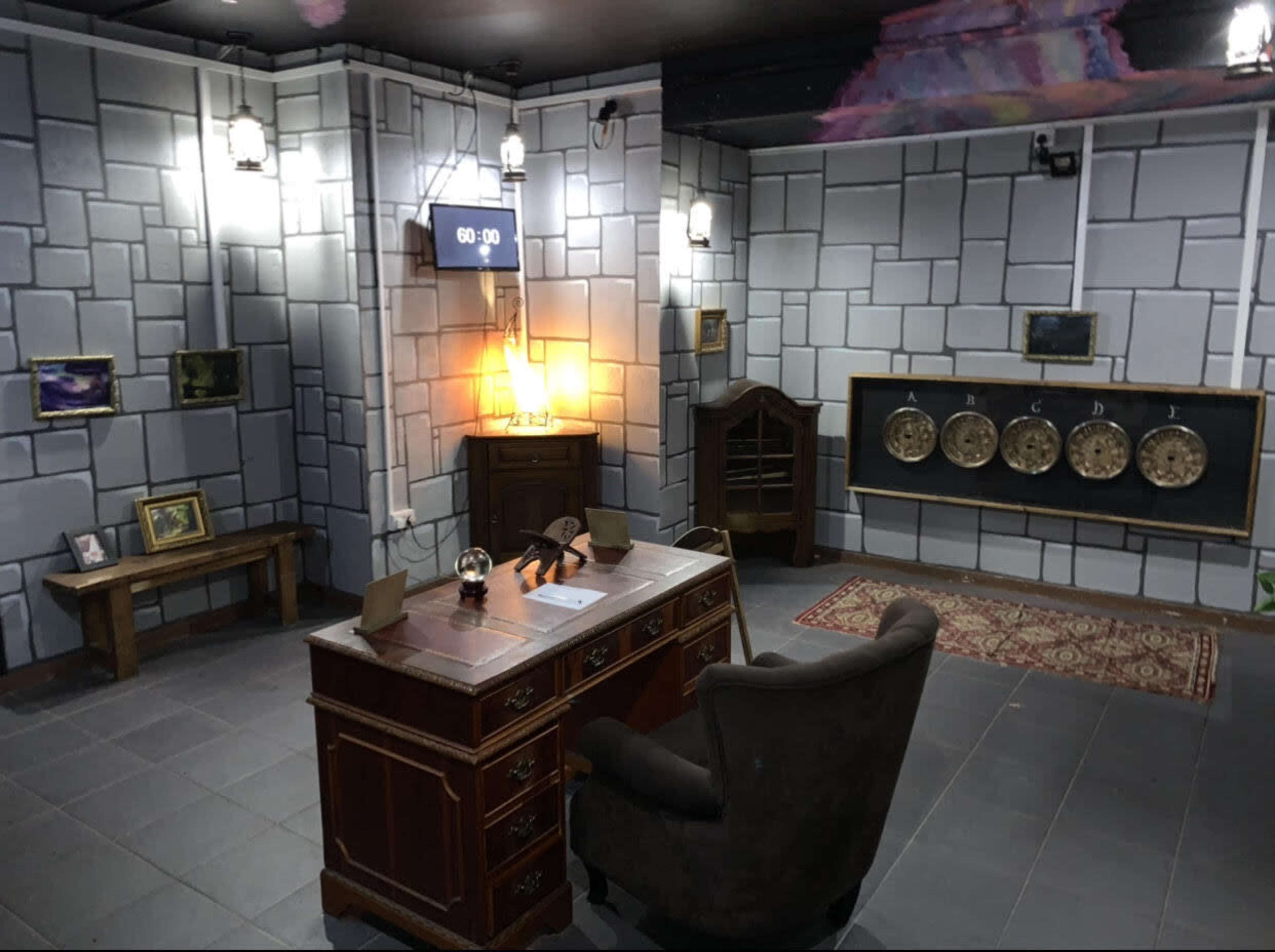 An escape room setup featuring a wooden desk with a chair, a clock displaying 60:00, and various decorative elements on the walls, including photographs and a display of circular items.