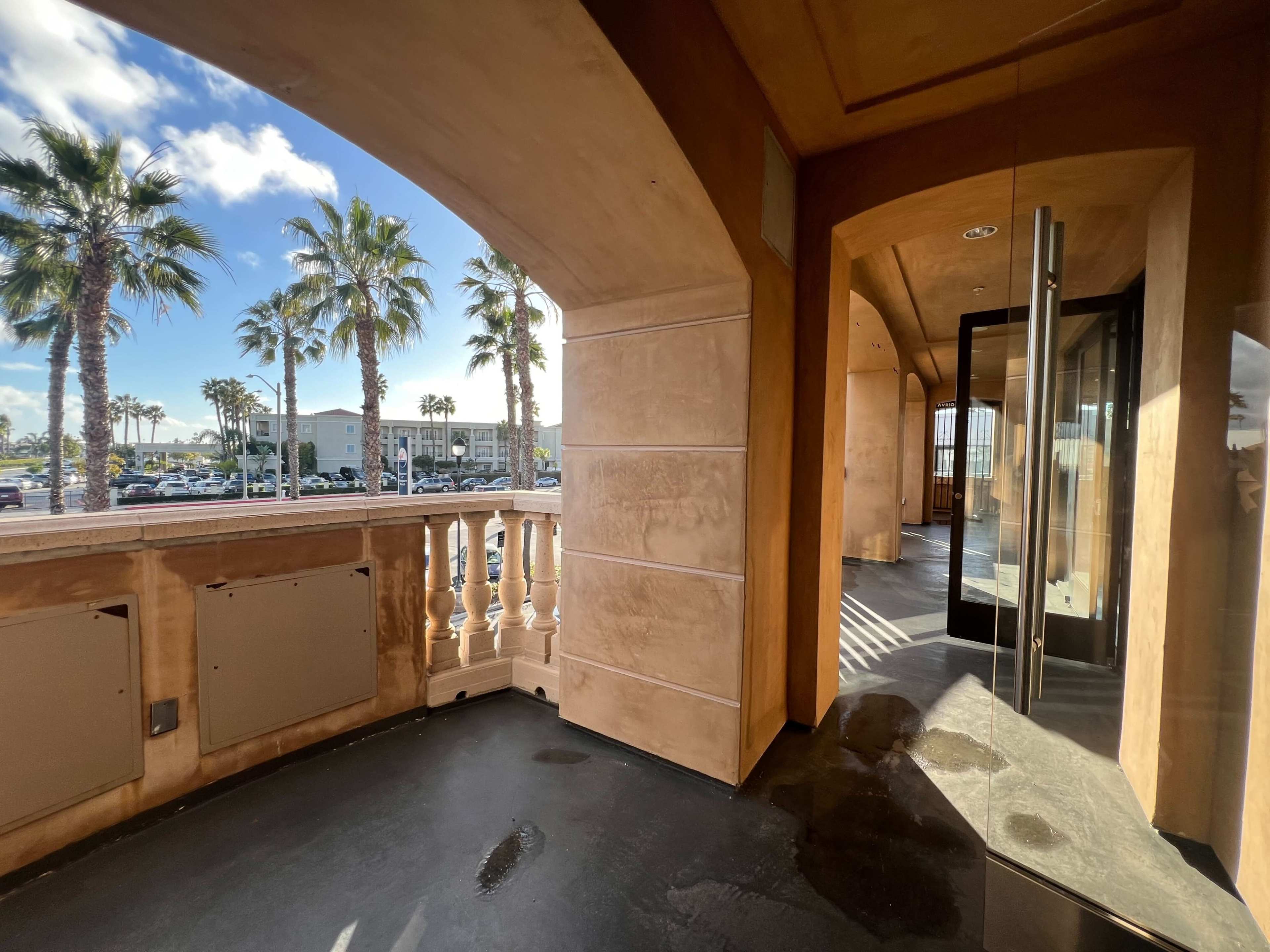 A spacious balcony area with a view of palm trees and a parking lot beyond.