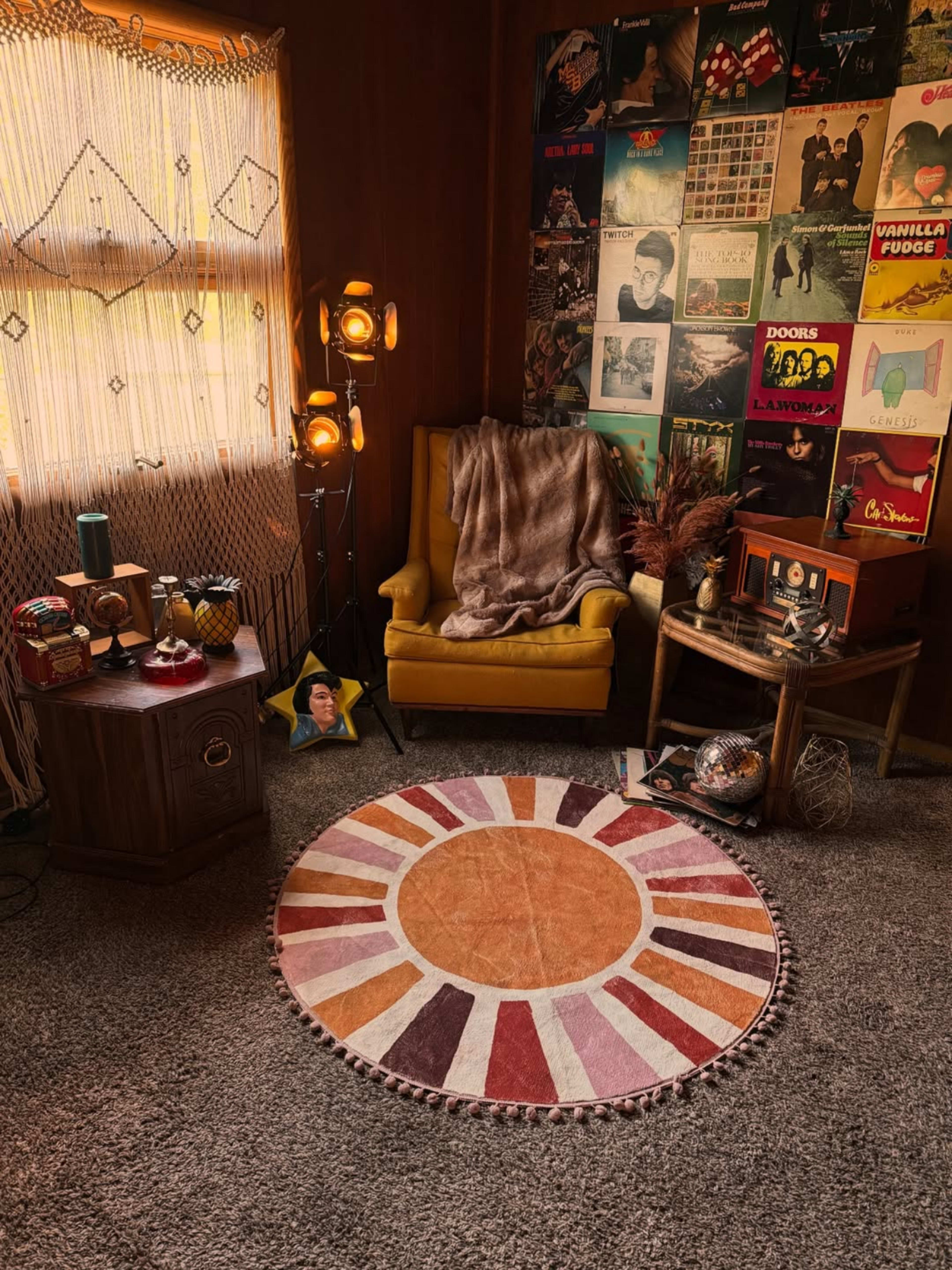The scene features a cozy room with a yellow armchair, a patterned round rug, a record collection on the wall, and a side table adorned with decorative items.