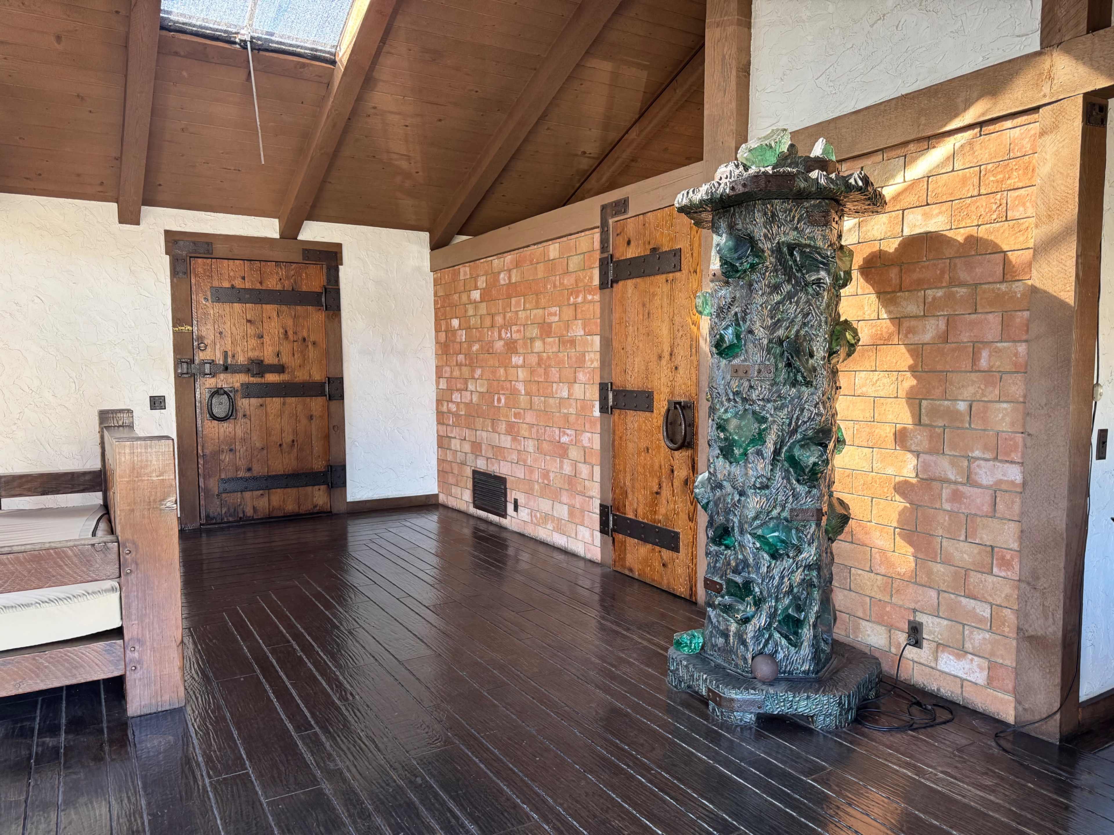 The image shows a wooden interior room with a vaulted ceiling, a brick wall, and a decorative green stone column.