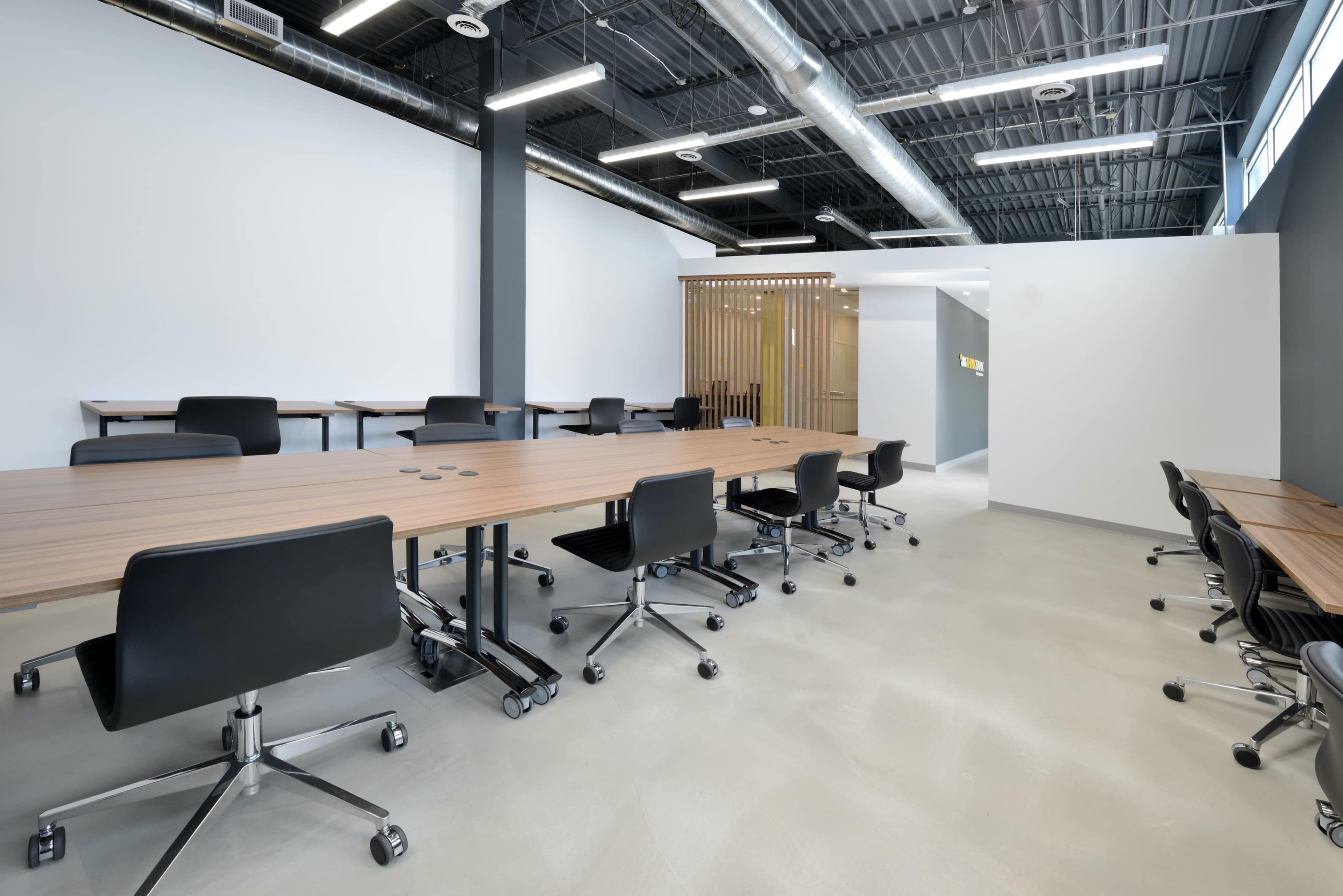 A modern conference room with long wooden tables and black swivel chairs arranged neatly.