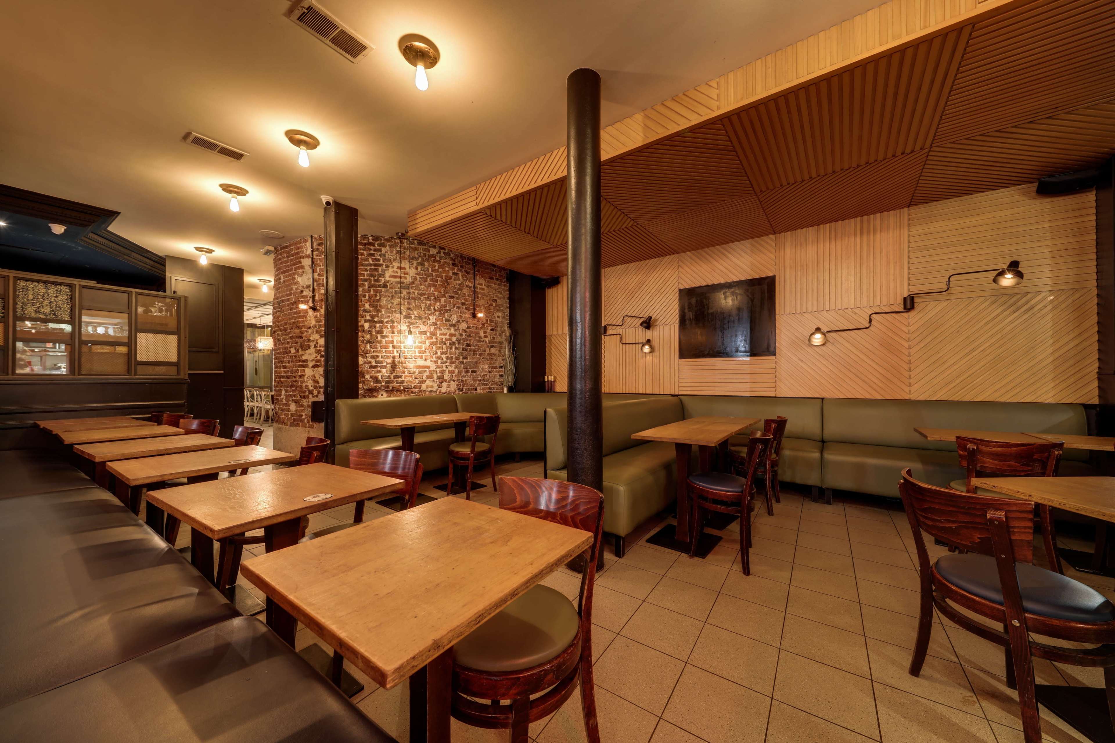 The image shows a restaurant interior with wooden tables, green seating booths, and exposed brick walls.