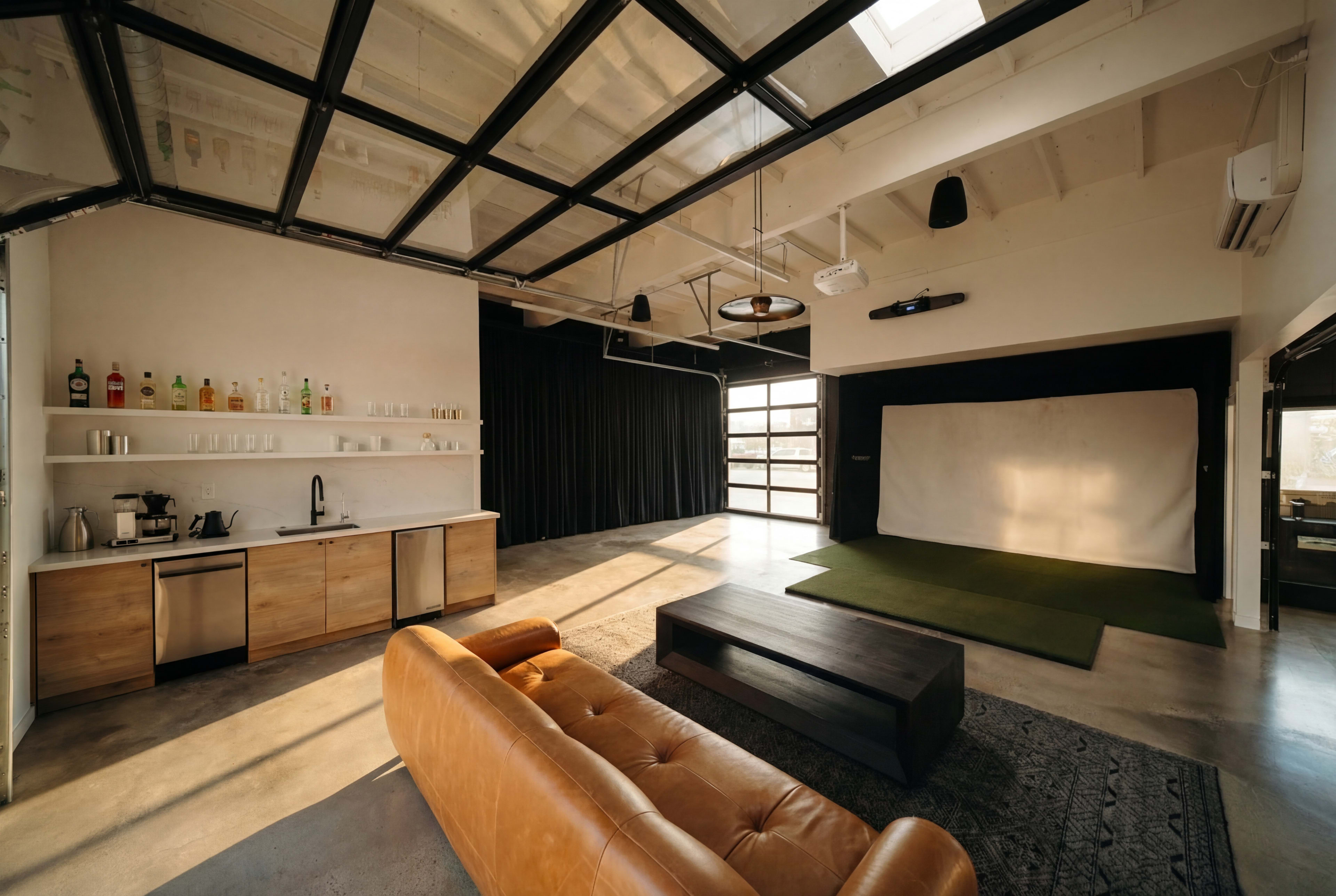 The image shows a spacious interior with a leather sofa, a wooden kitchenette, and a section of green carpeting set against a backdrop of black curtains and a white wall.