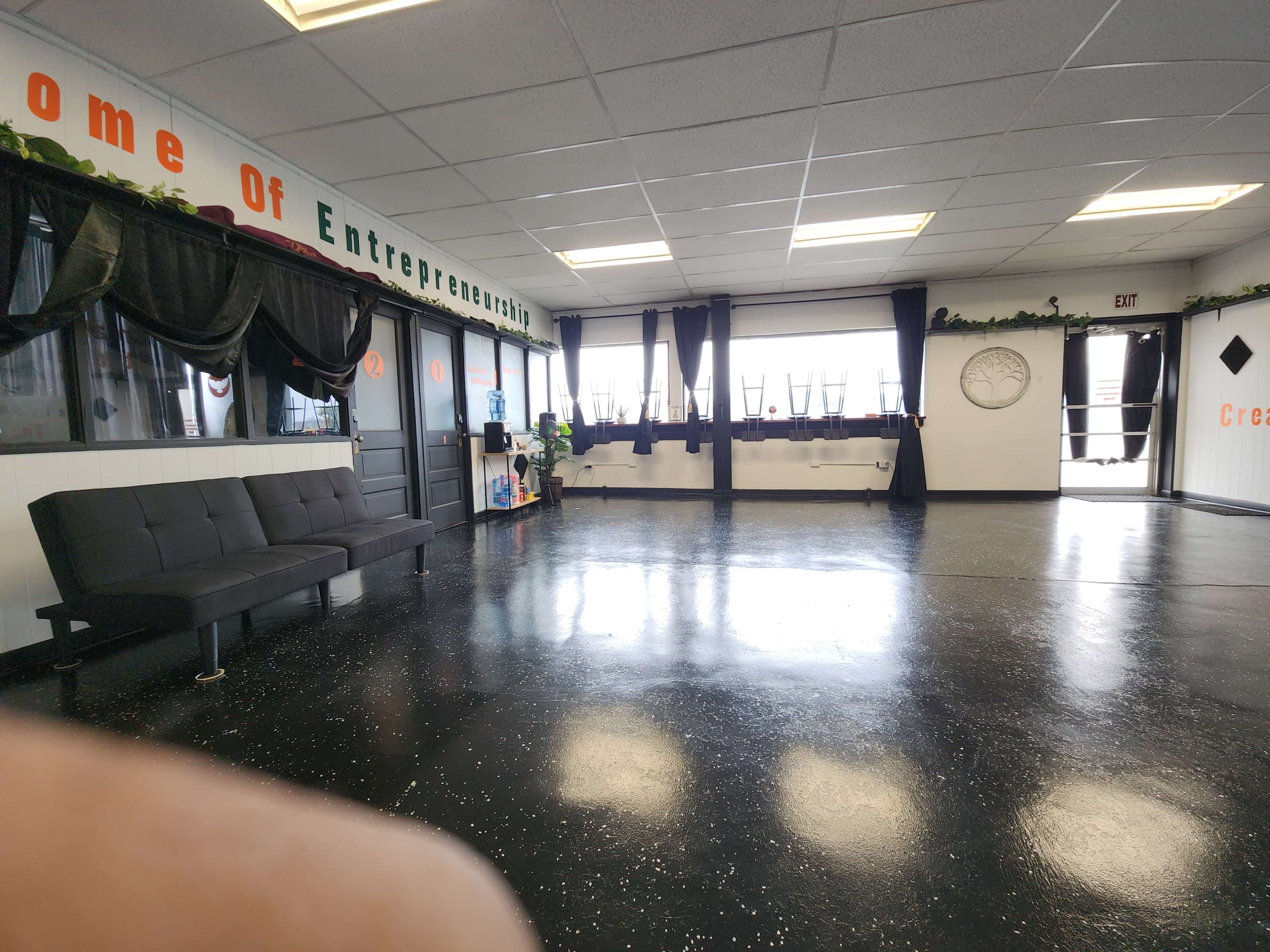 A spacious, vacant room with a black couch, large windows, and minimal decorations.