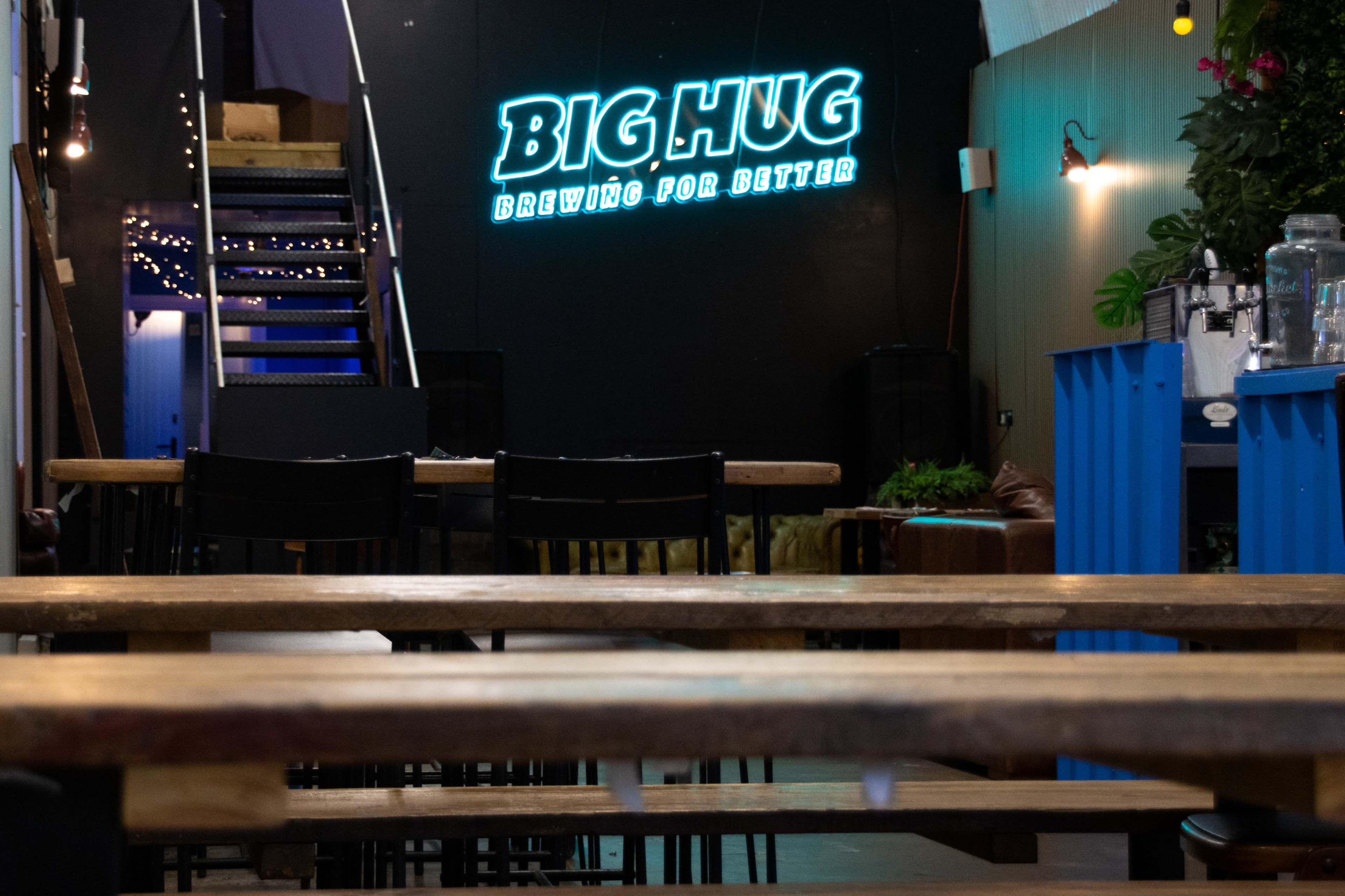 The interior of a café features wooden tables and a neon sign that reads "BIG HUG" on a black wall.