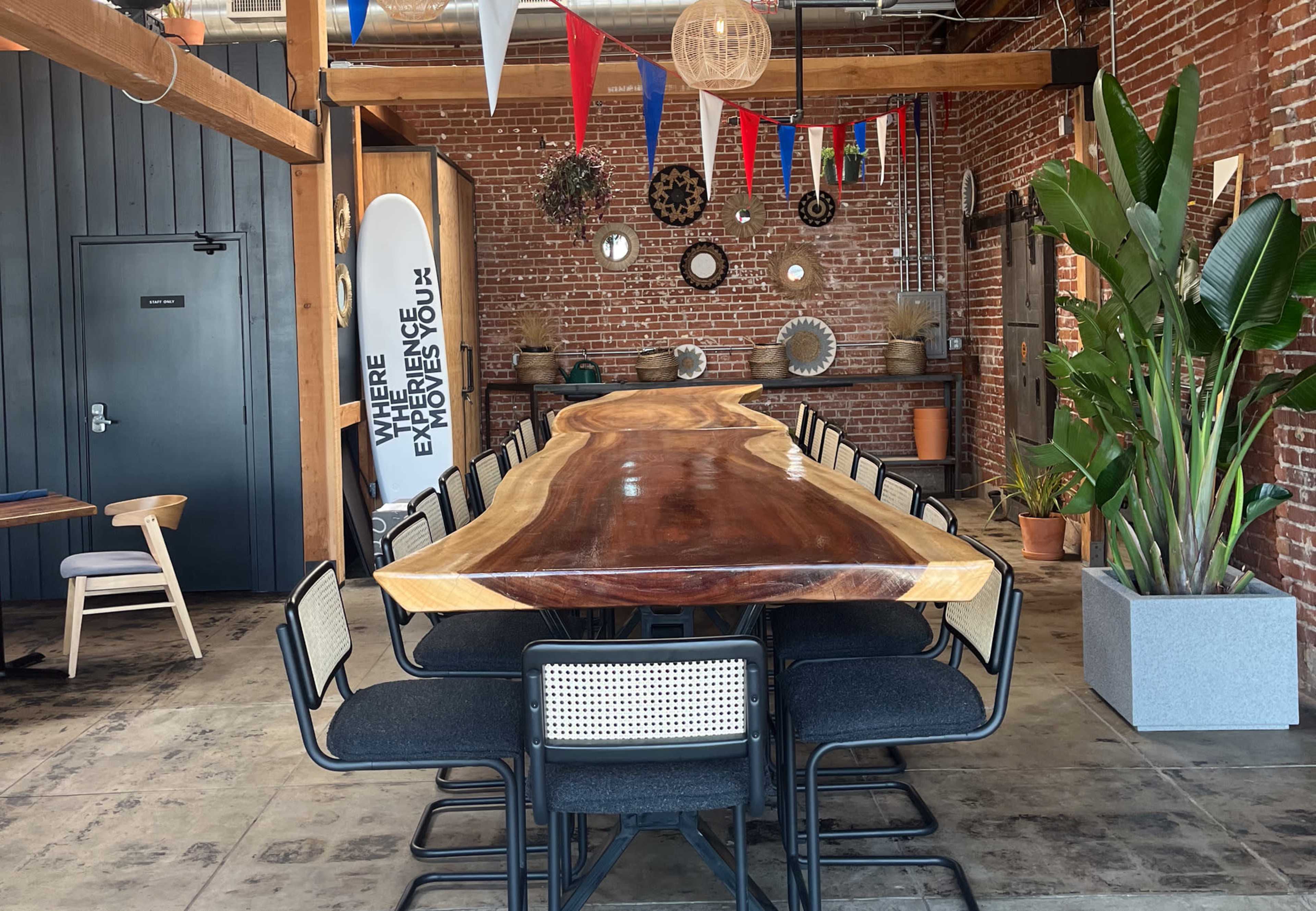 A long wooden table surrounded by black chairs in a spacious room with brick walls and various decorative elements.