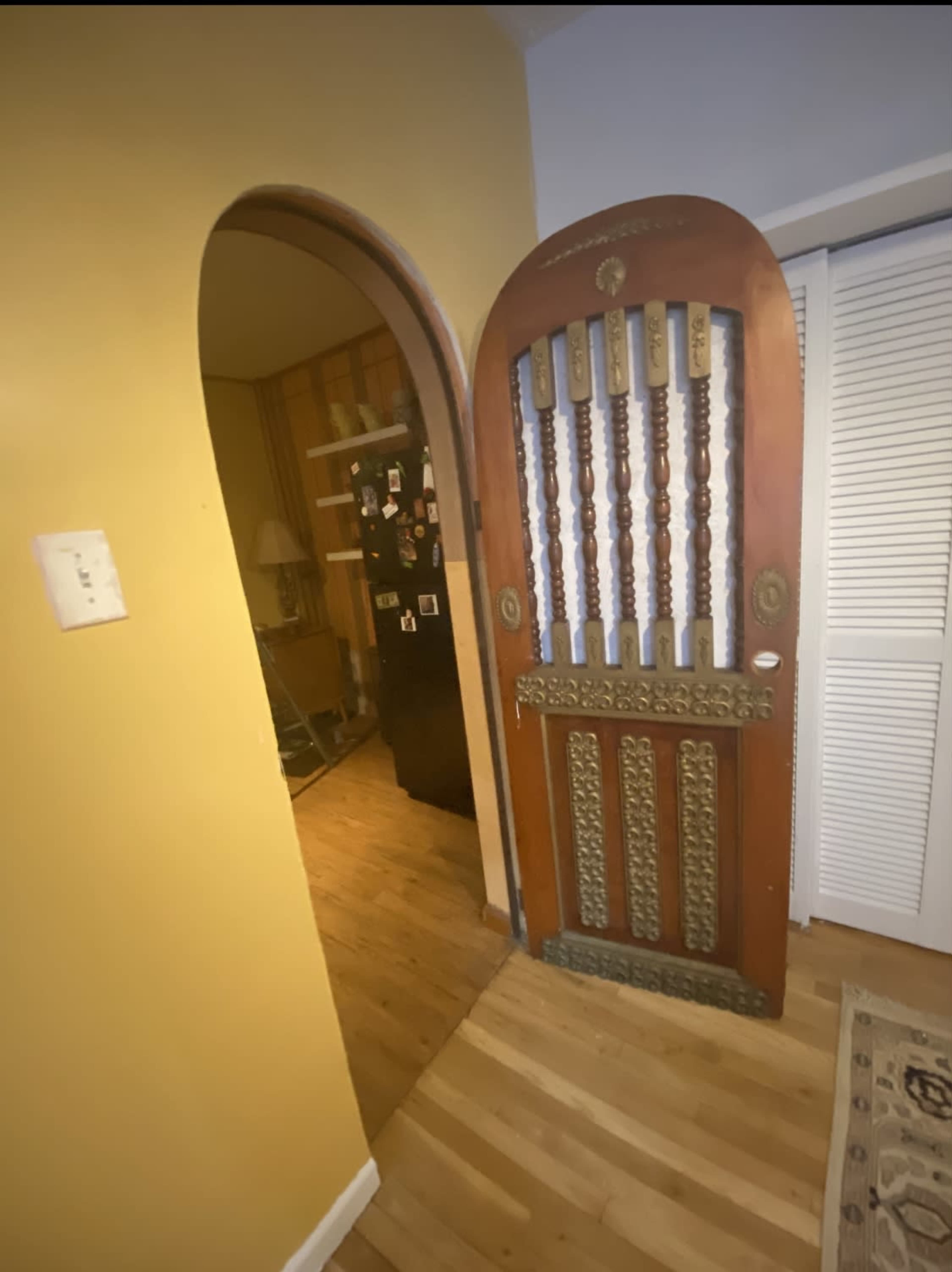 A wooden door with decorative metalwork, opening into a room with yellow walls and wooden flooring.