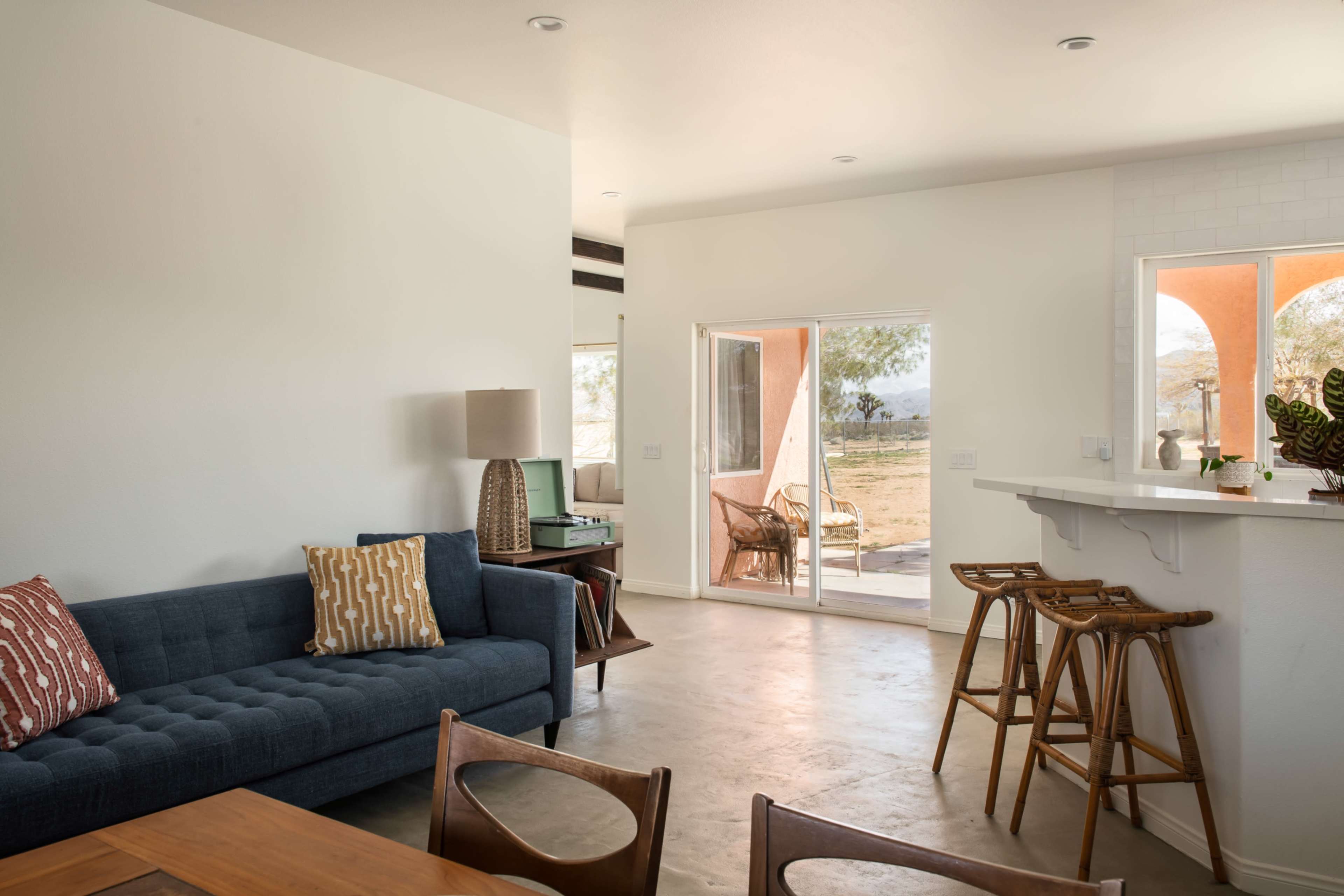 A modern, minimalist living space with a blue couch, a wooden dining table, and large windows that open to an outdoor view.