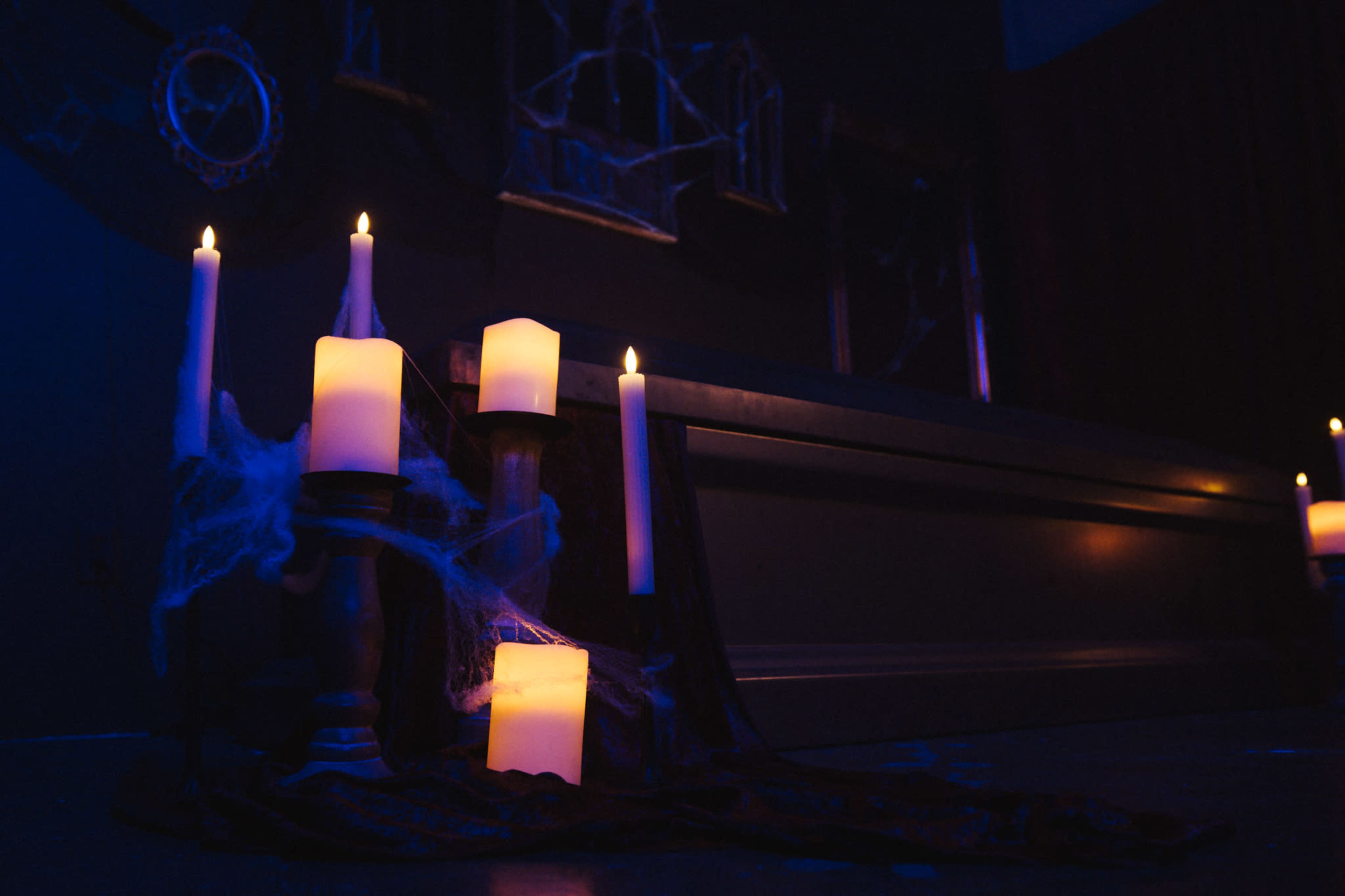 Candles of varying heights are arranged on a dark surface, surrounded by cobwebs and illuminated by blue lighting.