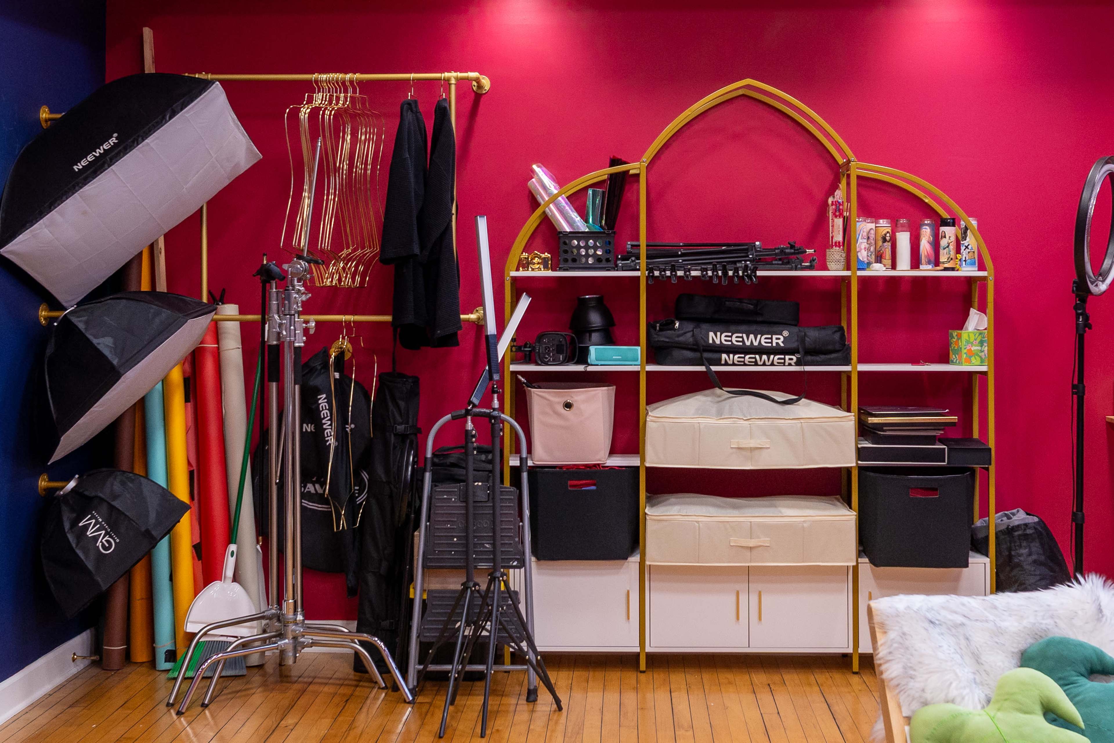 The image shows a colorful studio space with various photography equipment, including light stands, umbrellas, a shelving unit with boxes, and a display of backdrops.