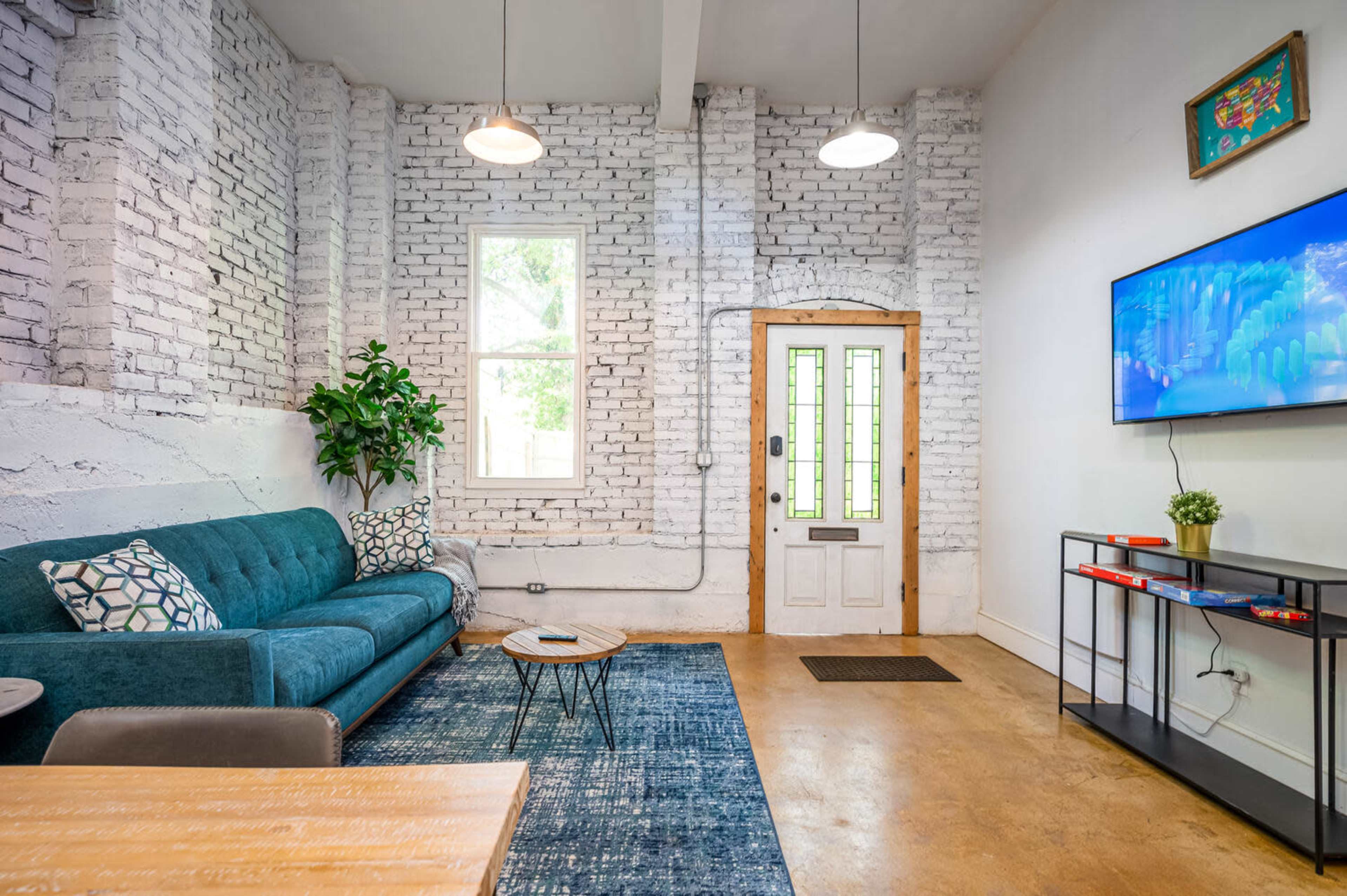 A modern living room with a teal sofa, a wooden coffee table, a blue rug, and a wall-mounted TV next to a door with glass panels.