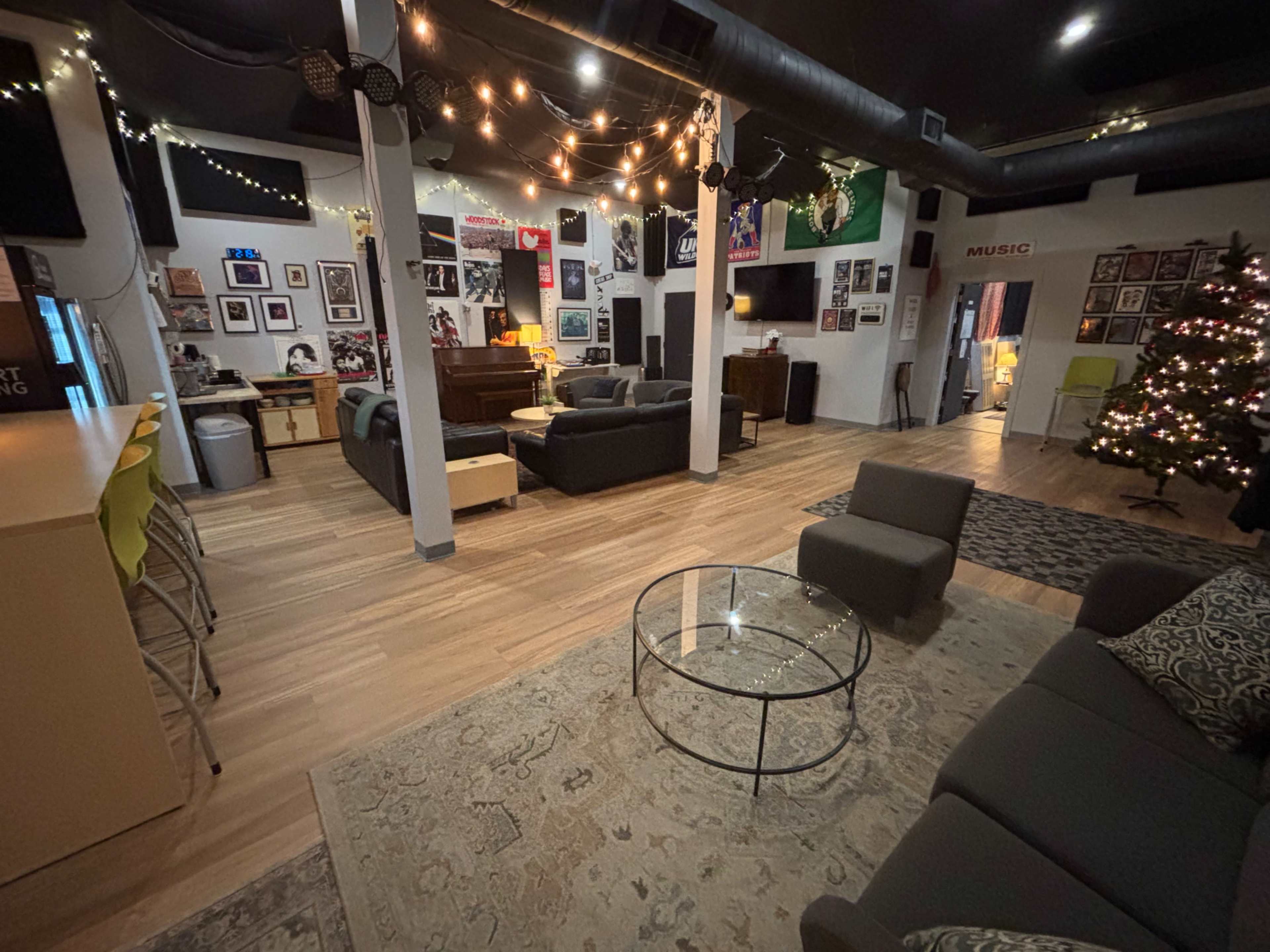 A spacious lounge area features comfortable seating, a large television, and decorative wall art, with a Christmas tree set up in the corner.