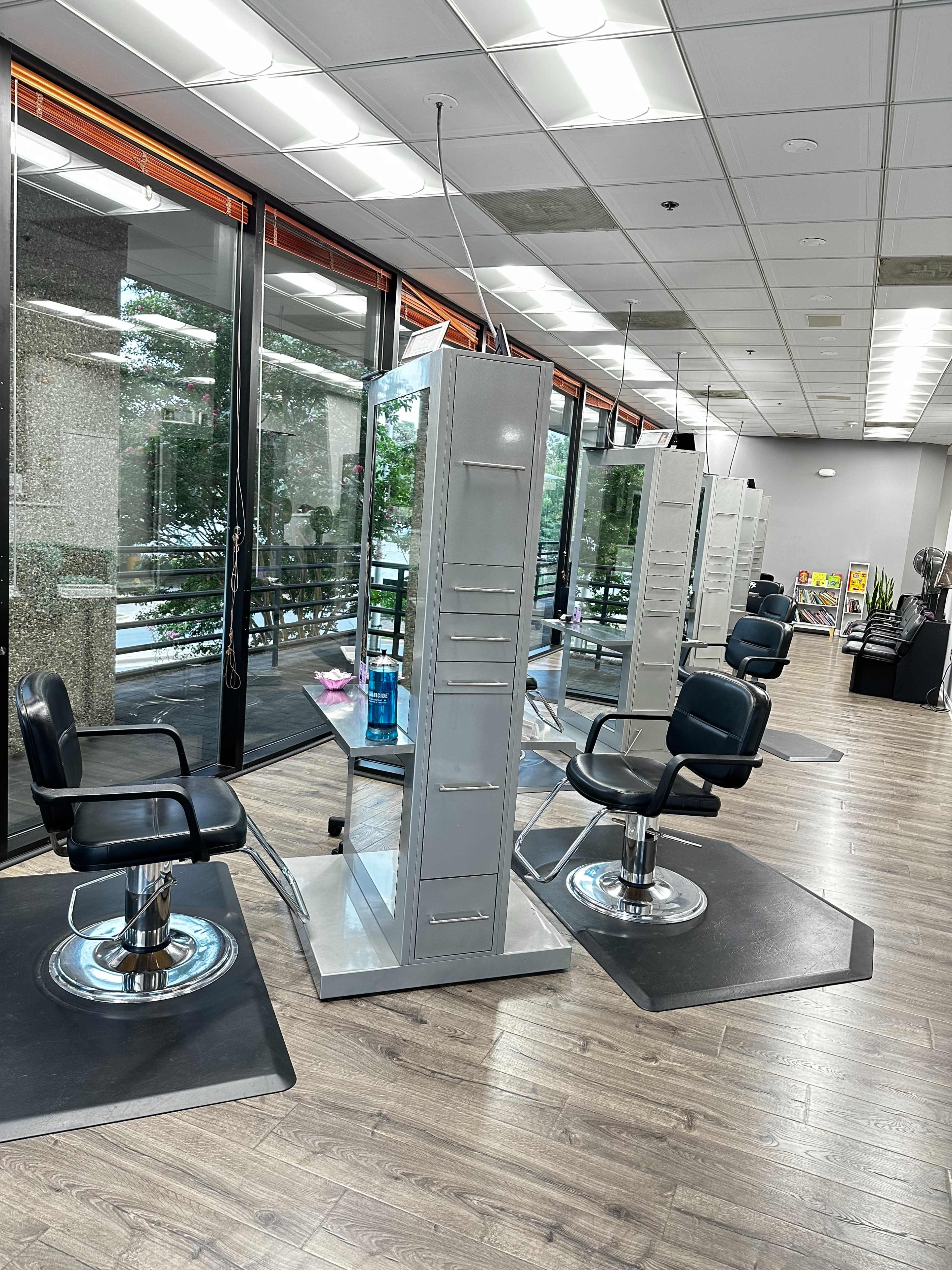 A well-lit hair salon with several styling stations featuring black salon chairs and tall mirrors.