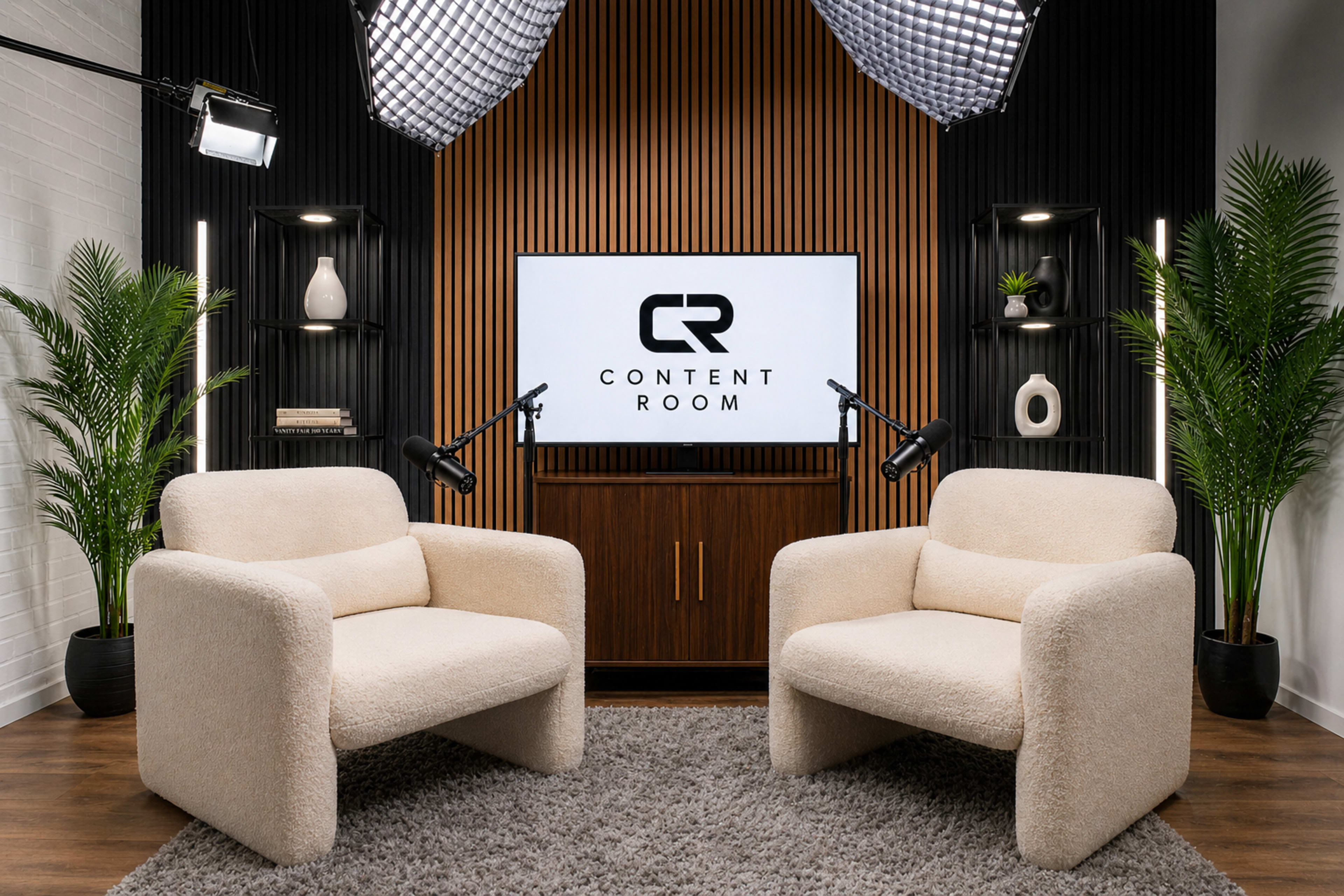 The image shows a modern content creation studio featuring two beige armchairs facing a large screen with the text "CONTENT ROOM" displayed, surrounded by decorative plants and studio lights.