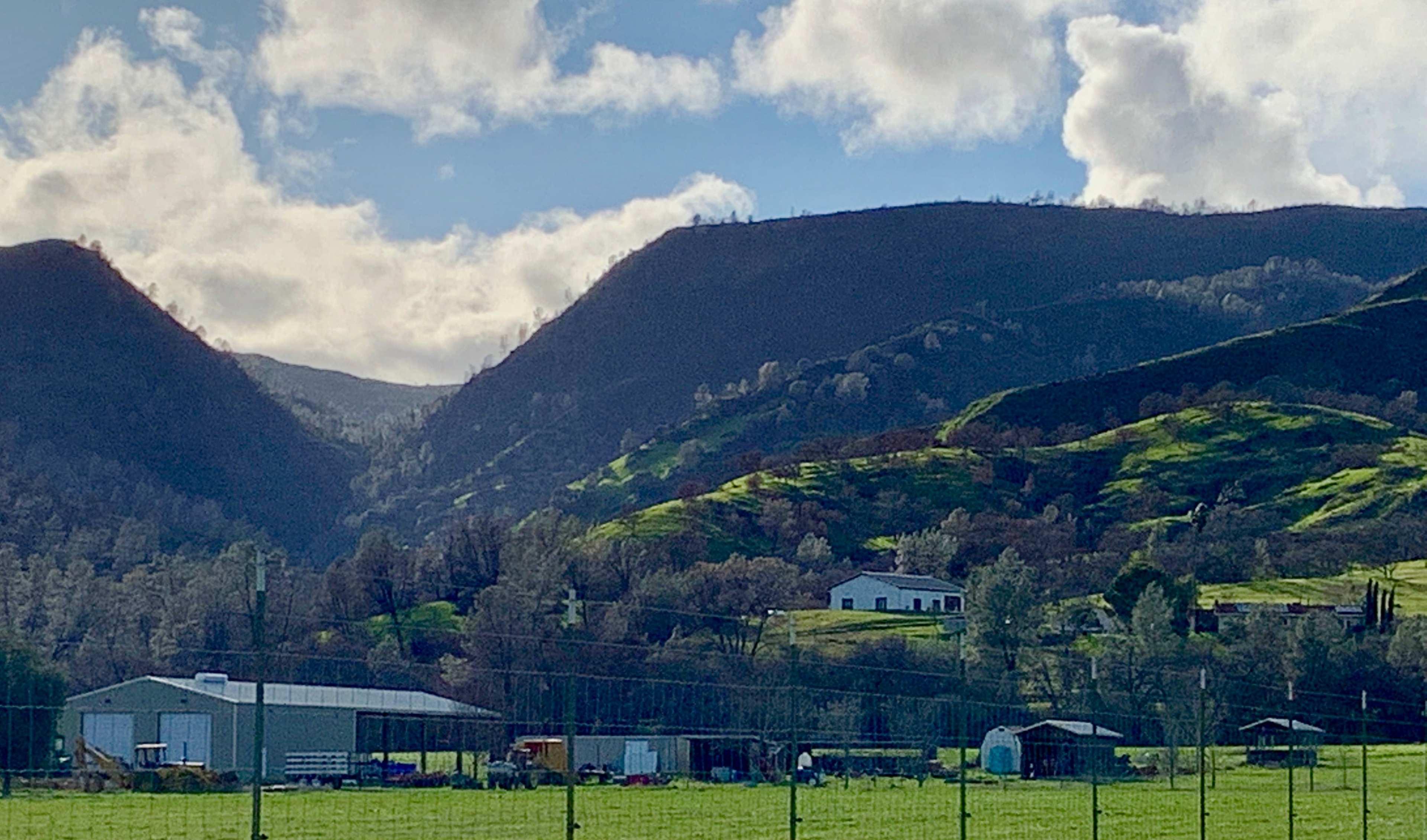 Green hills and mountains in the background with a farmhouse and several outbuildings in a rural landscape.