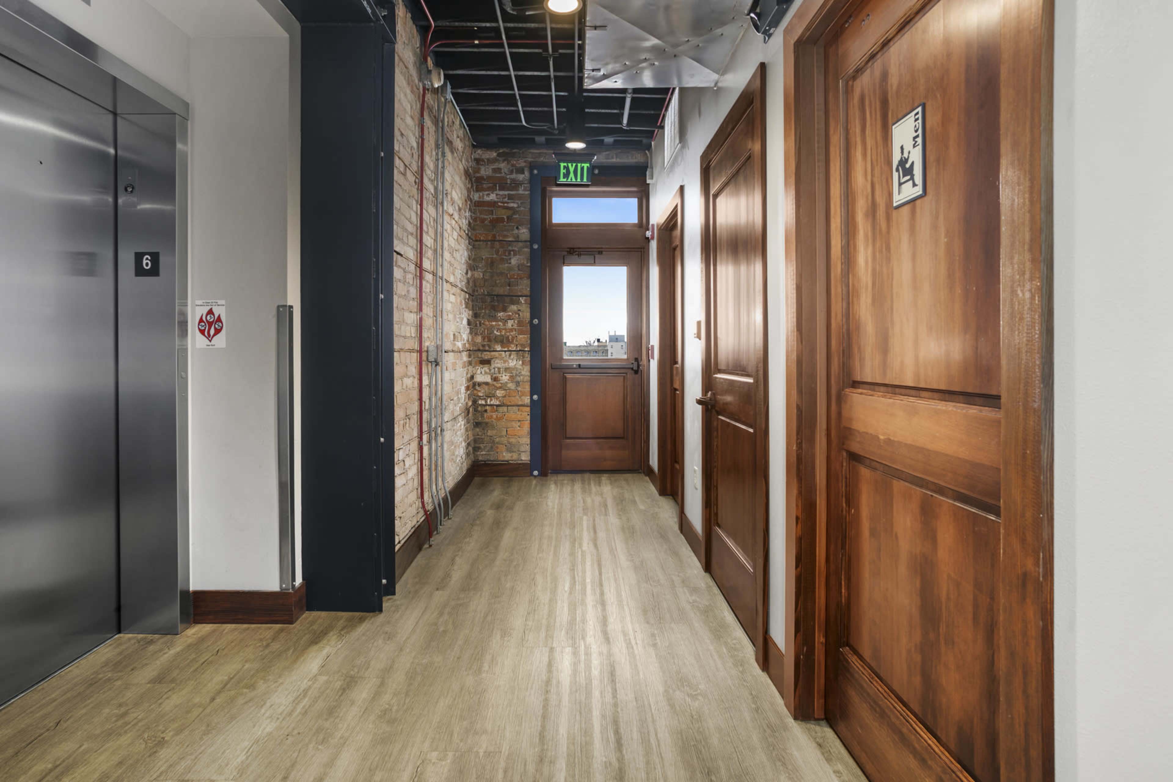 The image shows a corridor with wooden doors on both sides, an elevator at the left, and brick walls.