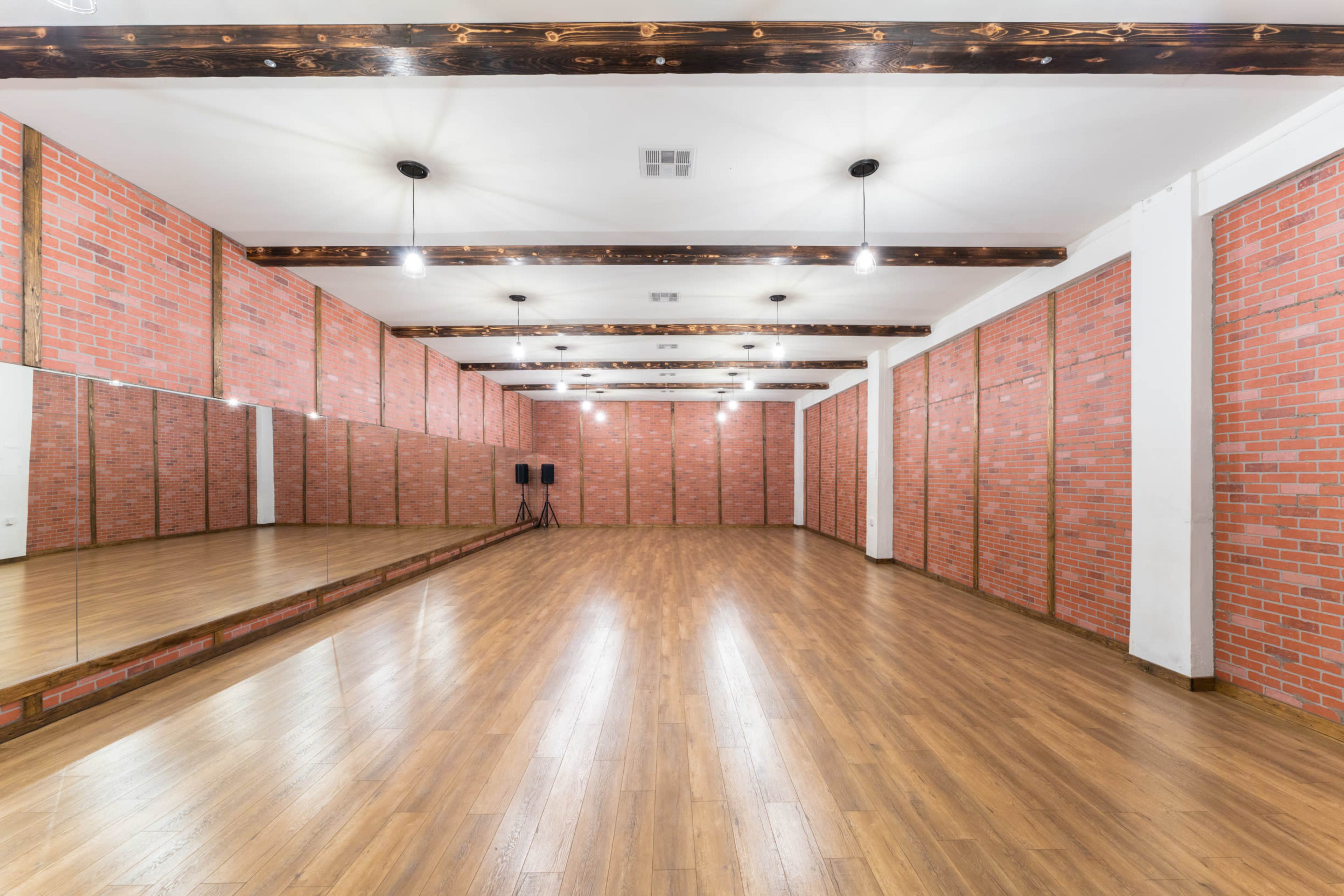 The image shows a spacious dance studio with exposed brick walls, a wooden floor, and a large mirrored wall.