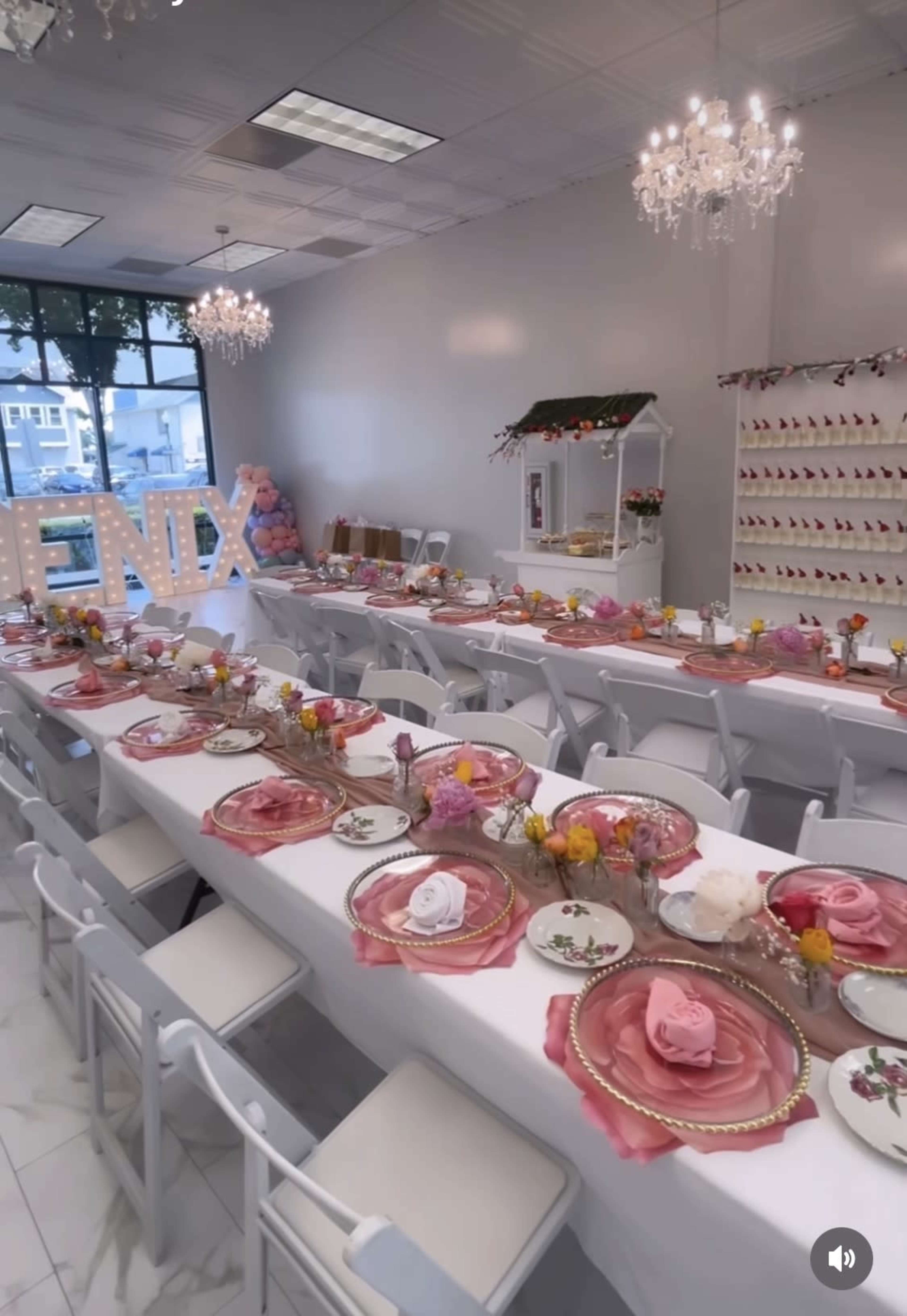 A brightly lit event space features long tables set with floral centerpieces and elegant place settings, adorned with decorative napkins.