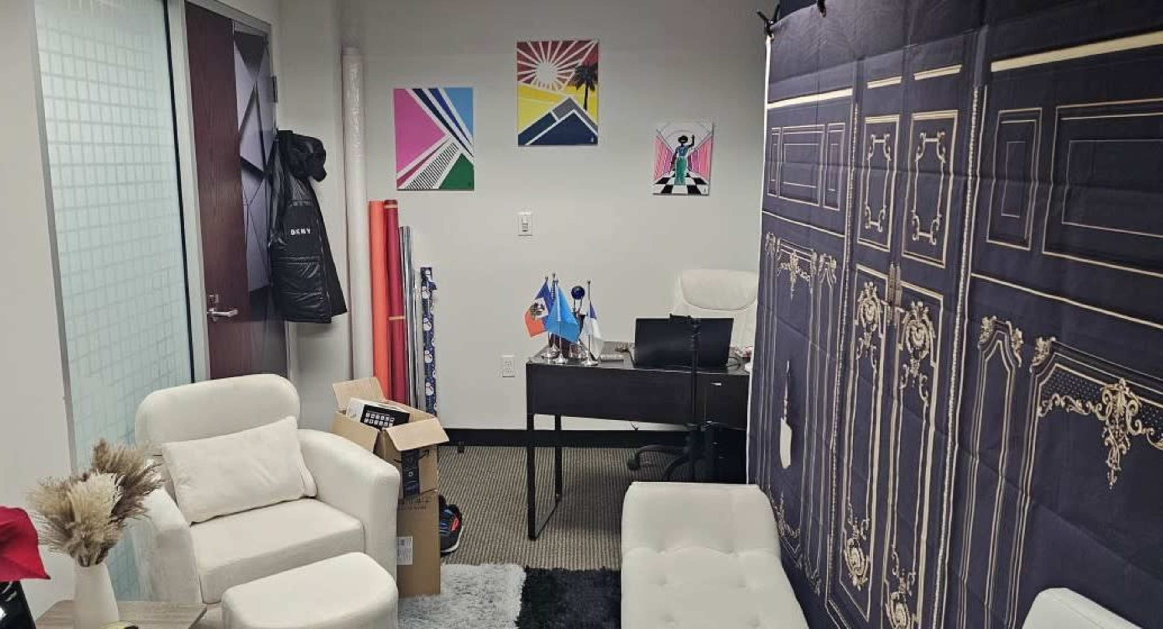 An office space with a desk, two white chairs, colorful wall art, and a backdrop featuring a door design.