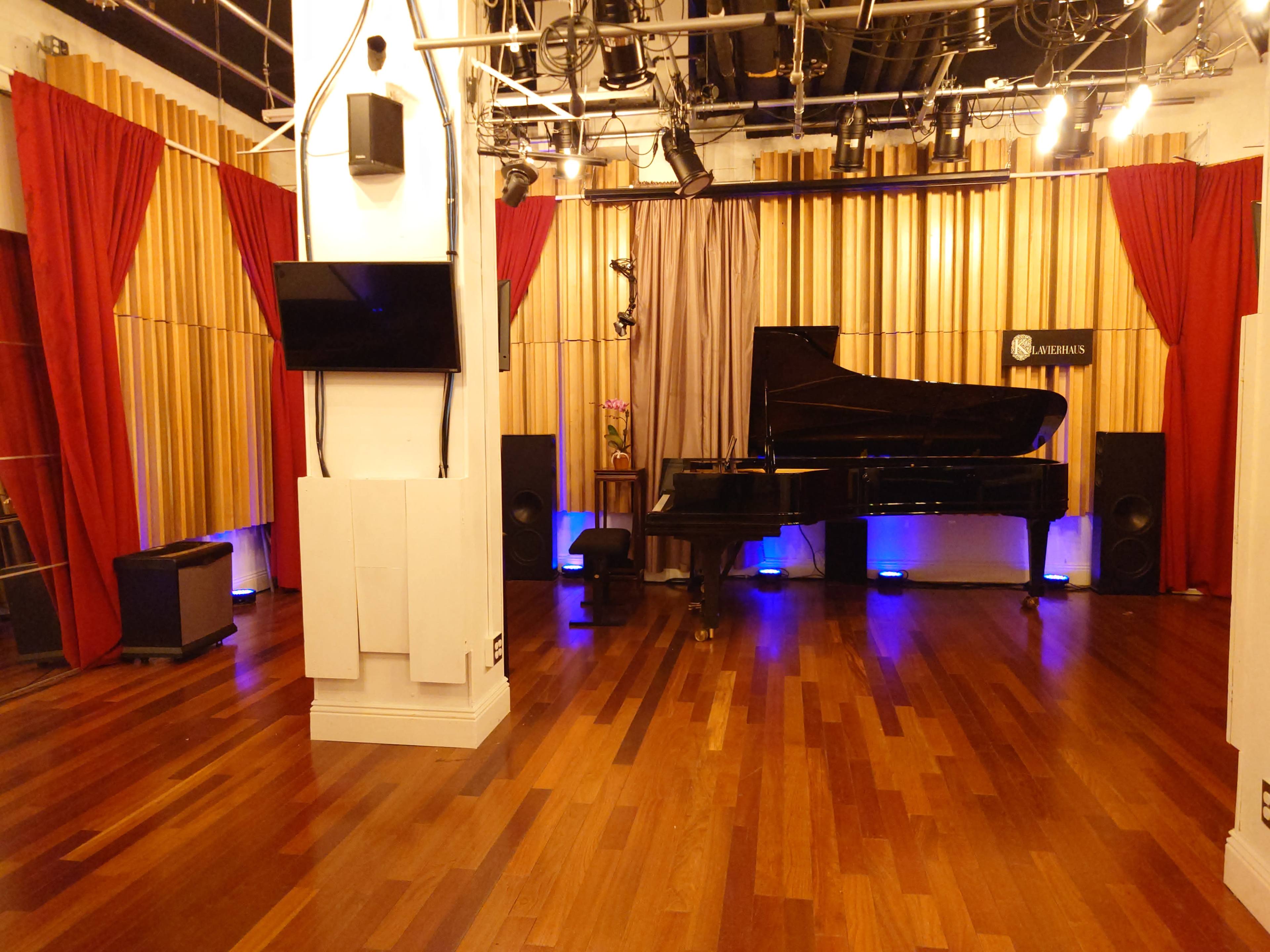 The image shows a music studio with a grand piano, wooden paneling, ambient lighting, and red curtains.