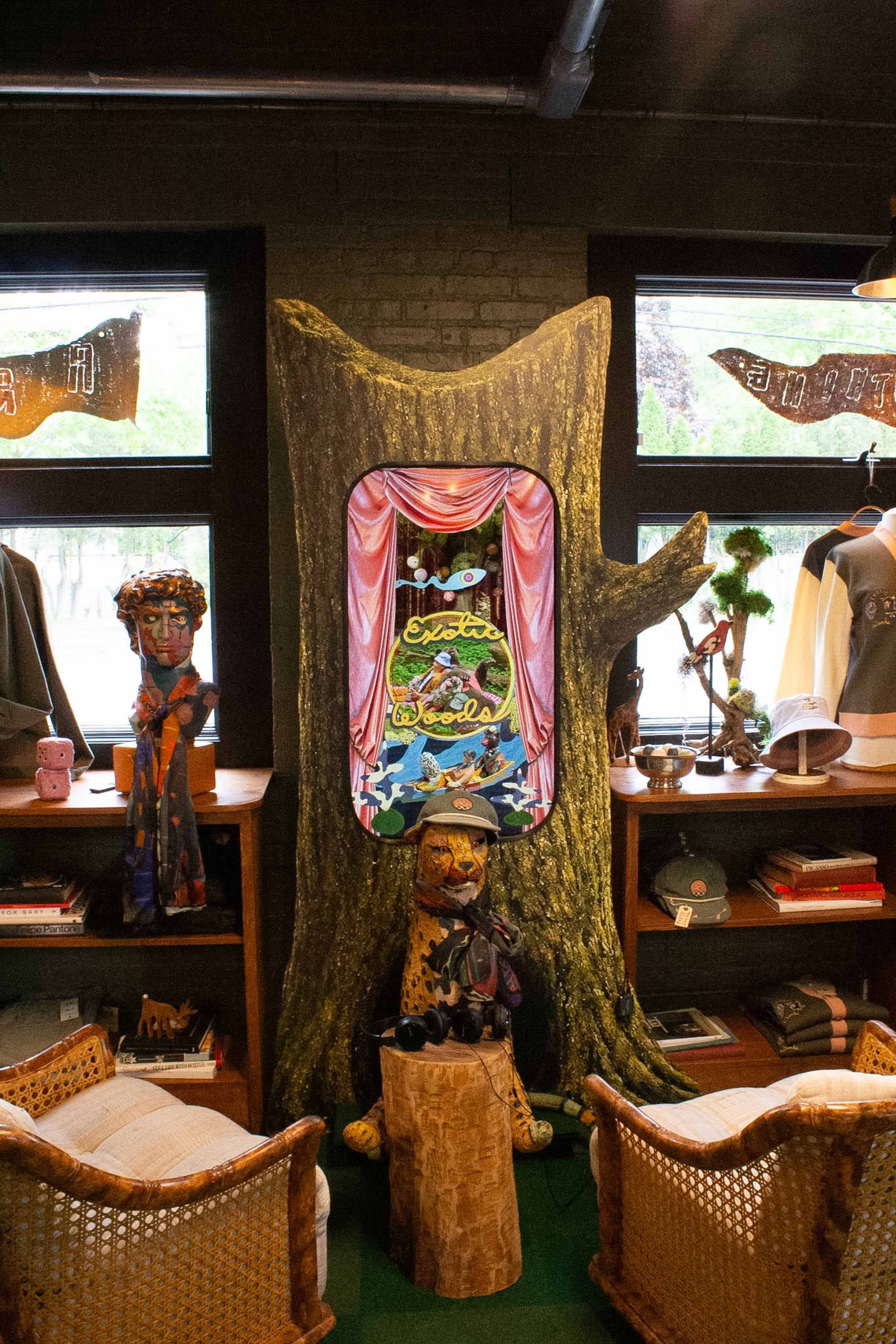 The image features a tree stump serving as a backdrop for colorful artwork, with an eclectic display of merchandise and decor arranged around it in a cozy retail space.