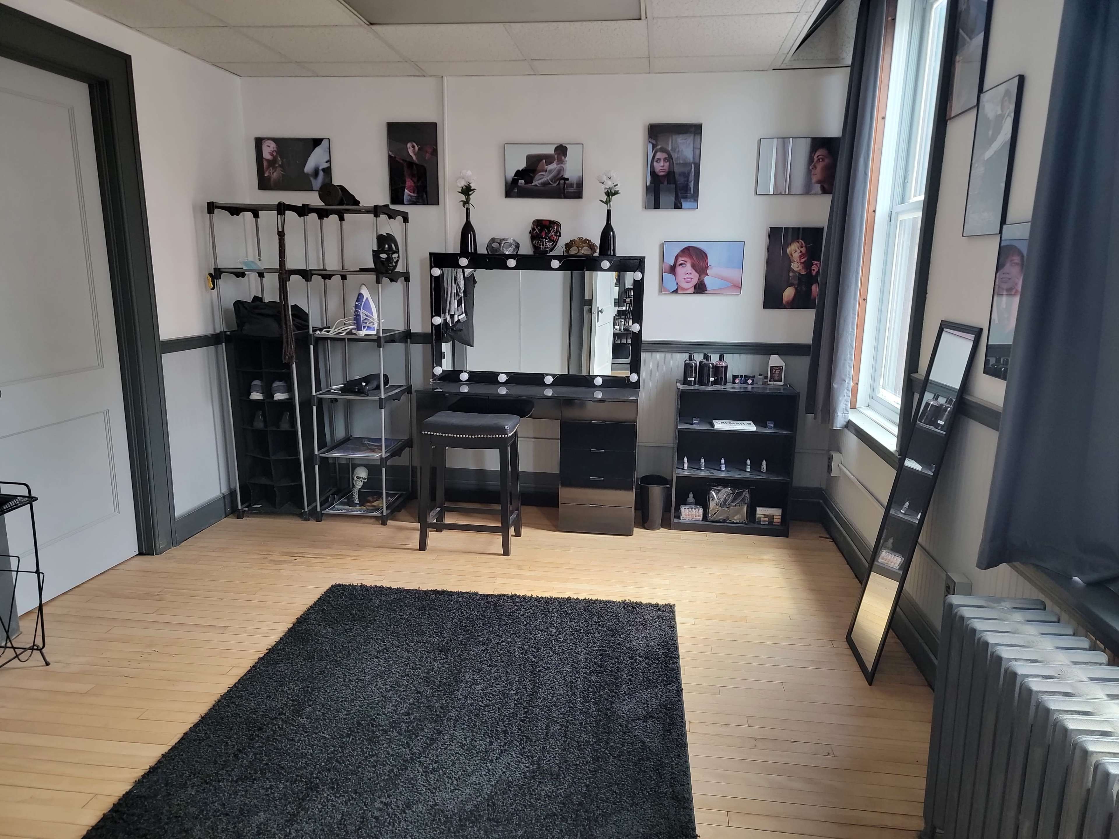 A room with a vanity desk, shelves filled with beauty products, framed photographs on the walls, and a large mirror against one side.