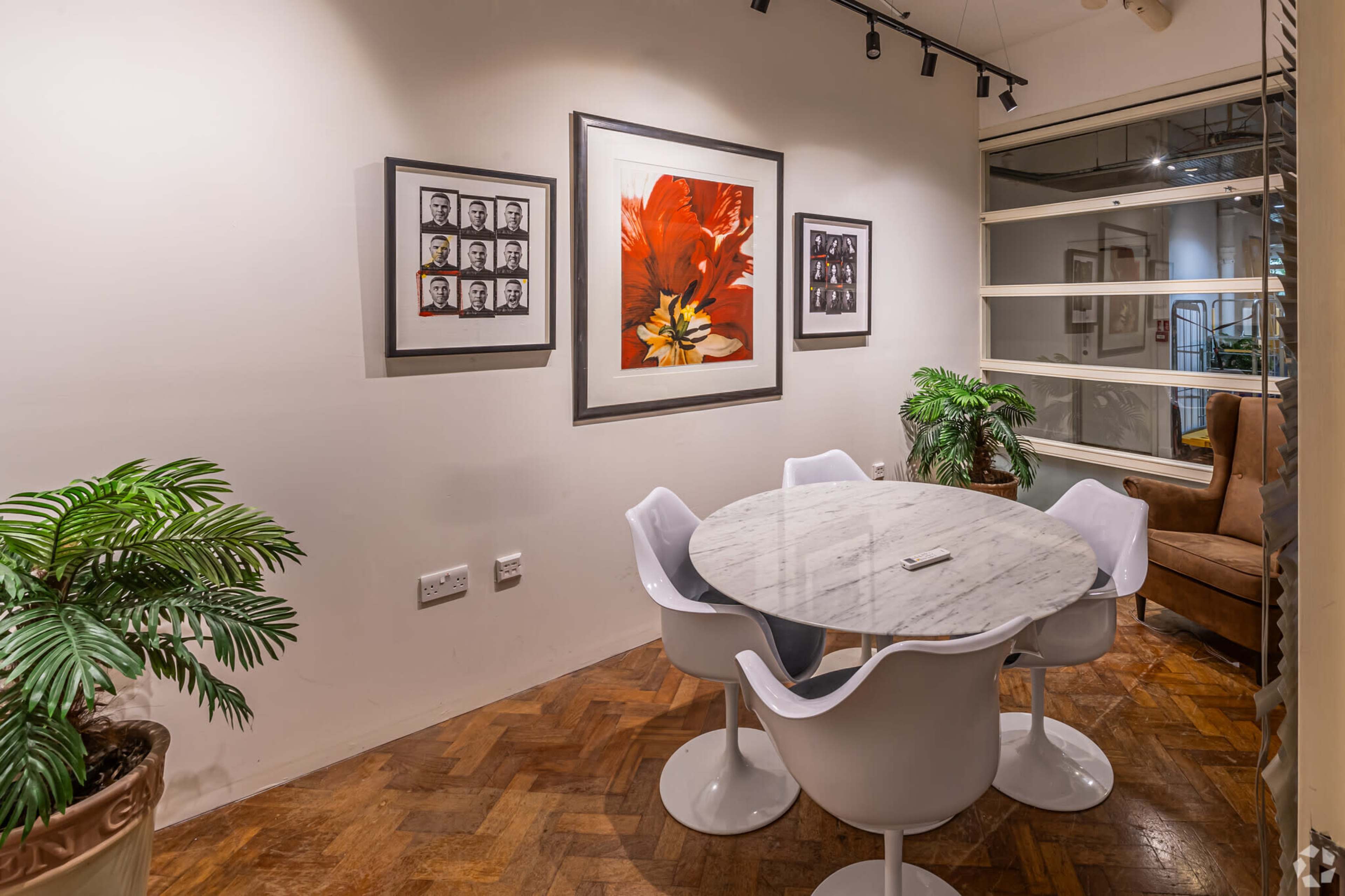A small dining area features a round marble table surrounded by white chairs, with framed artwork and potted plants on the walls.