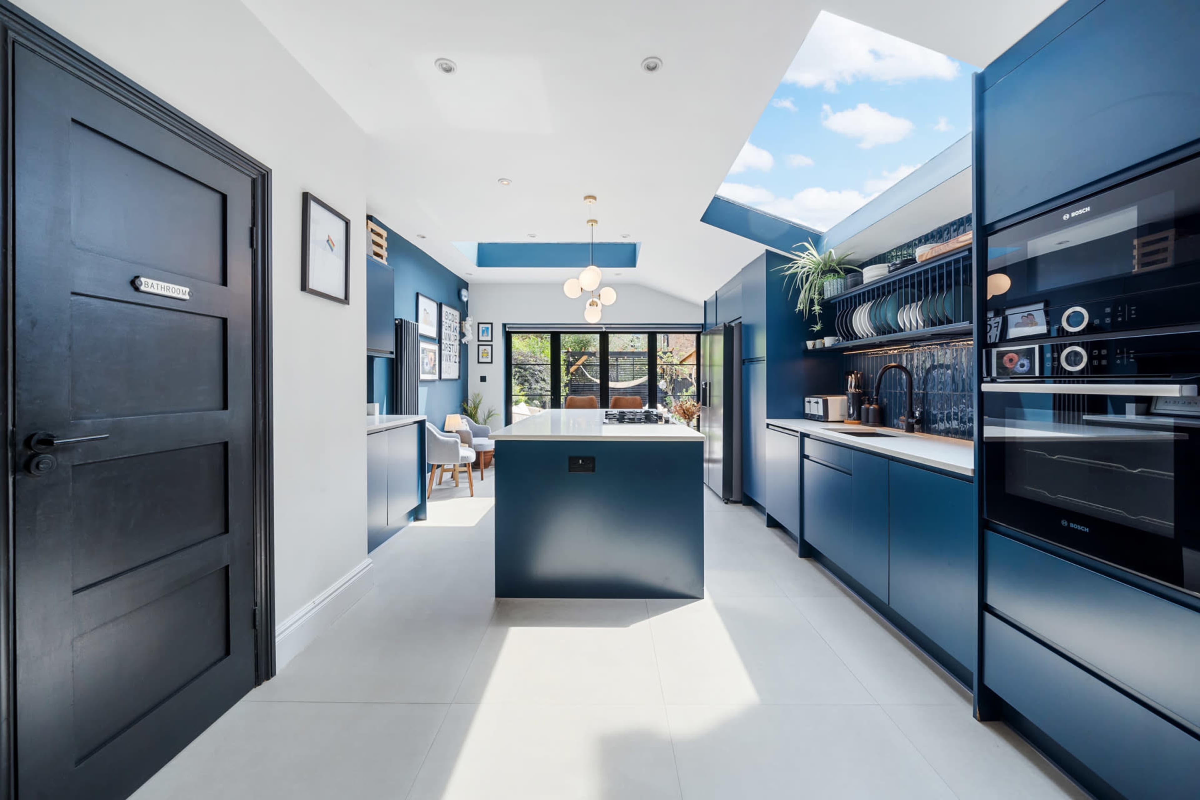 A modern kitchen featuring dark blue cabinetry, a central island, and large windows that allow natural light to fill the space.
