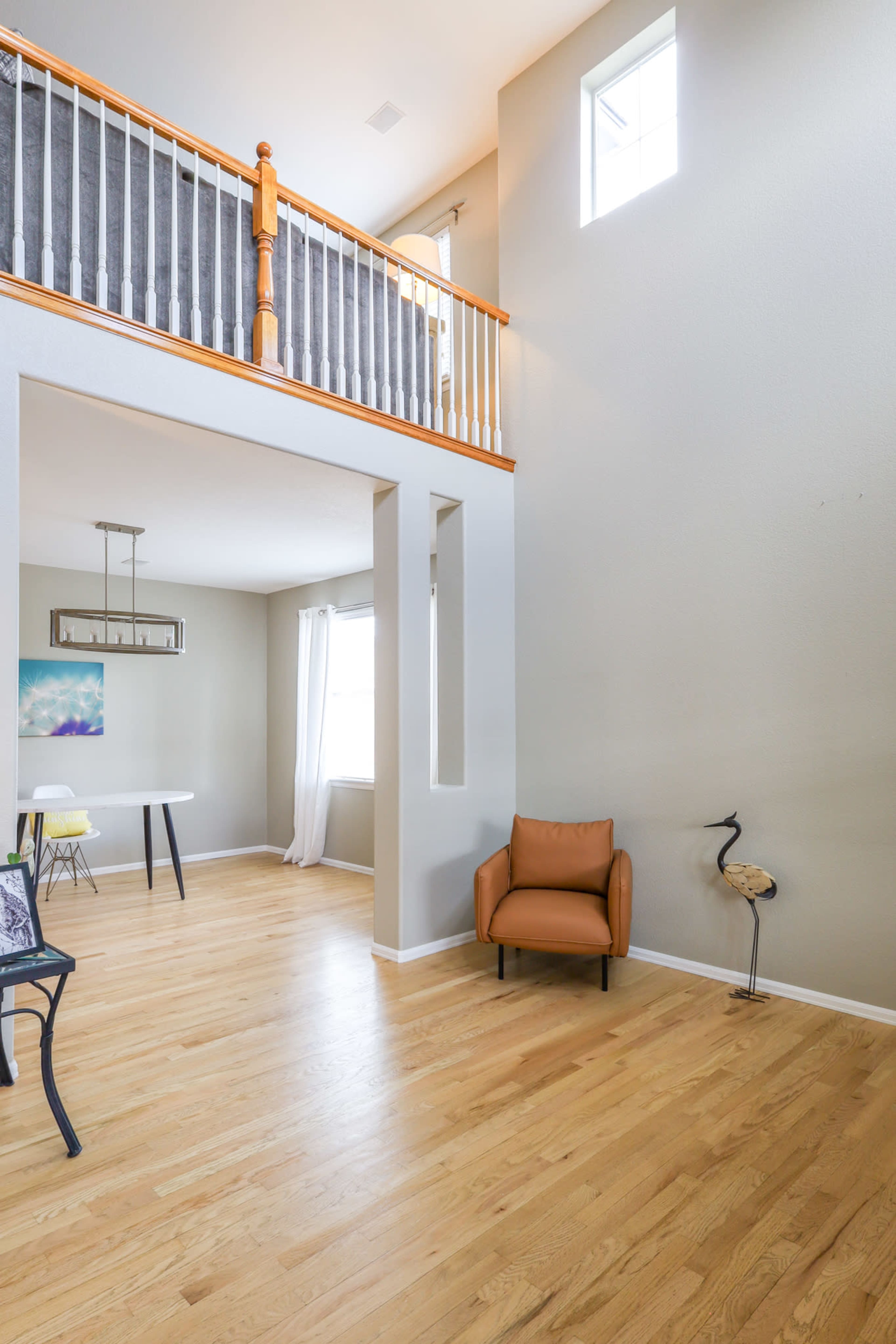 A spacious, well-lit interior with wooden floors, a dining table, a brown armchair, and a decorative figure near the wall.
