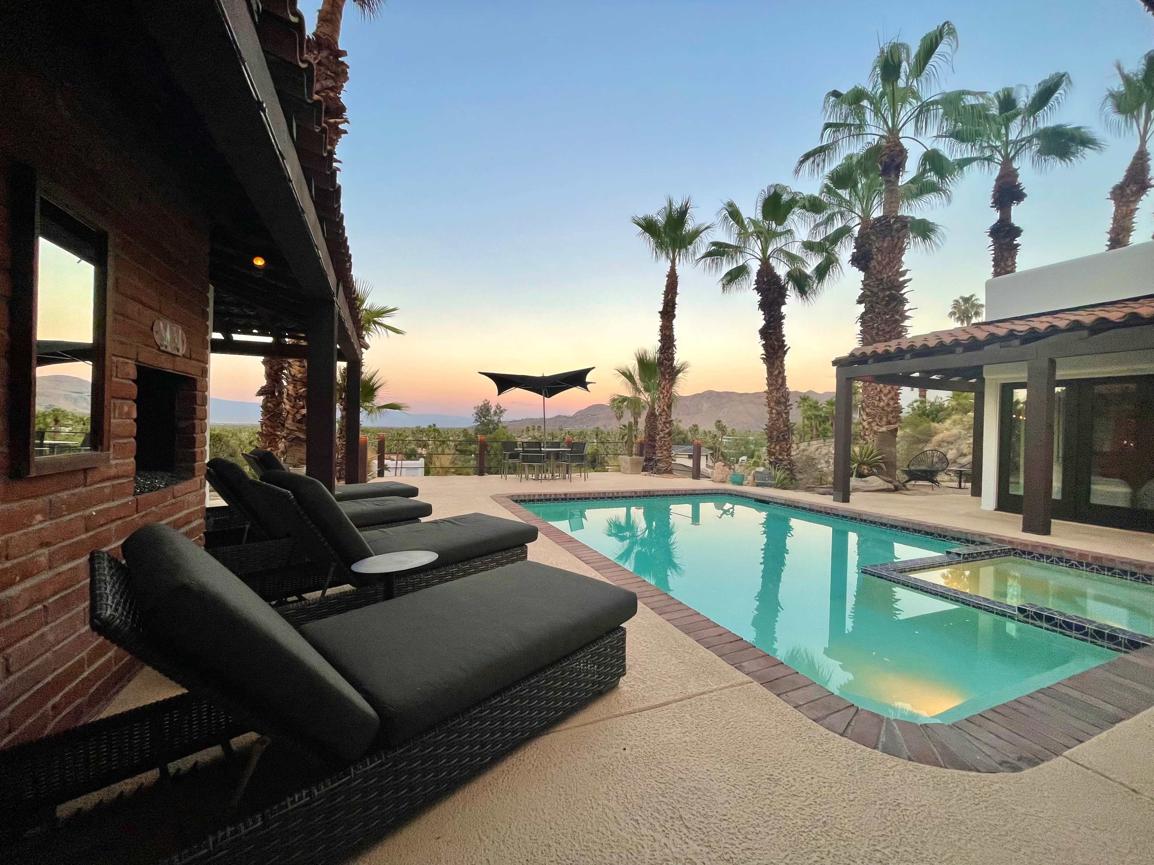 The scene features a swimming pool surrounded by palm trees and lounge chairs, with a view of a distant mountain at sunset.
