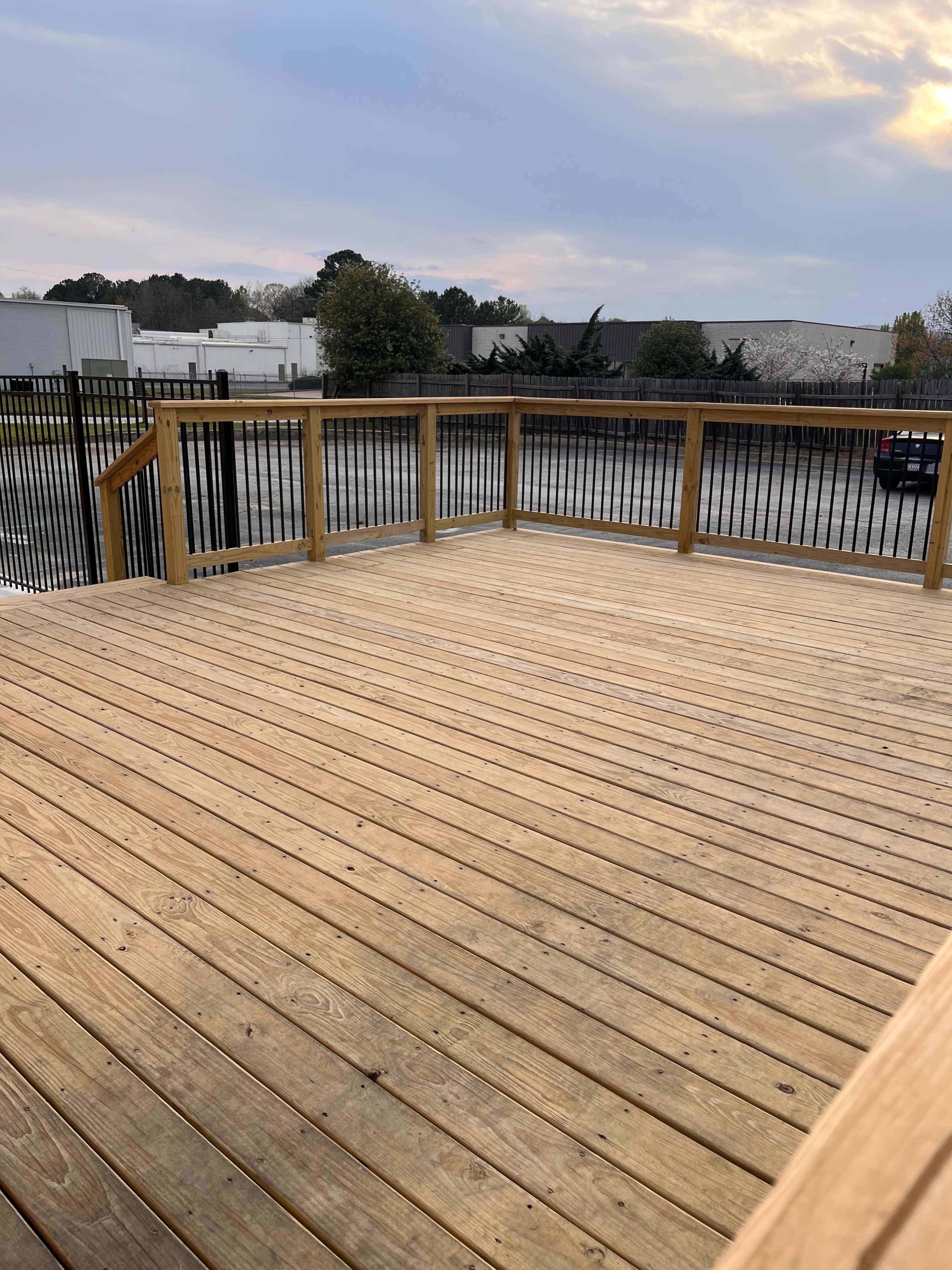 A wooden deck with a railing overlooks a parking lot and buildings in the background.